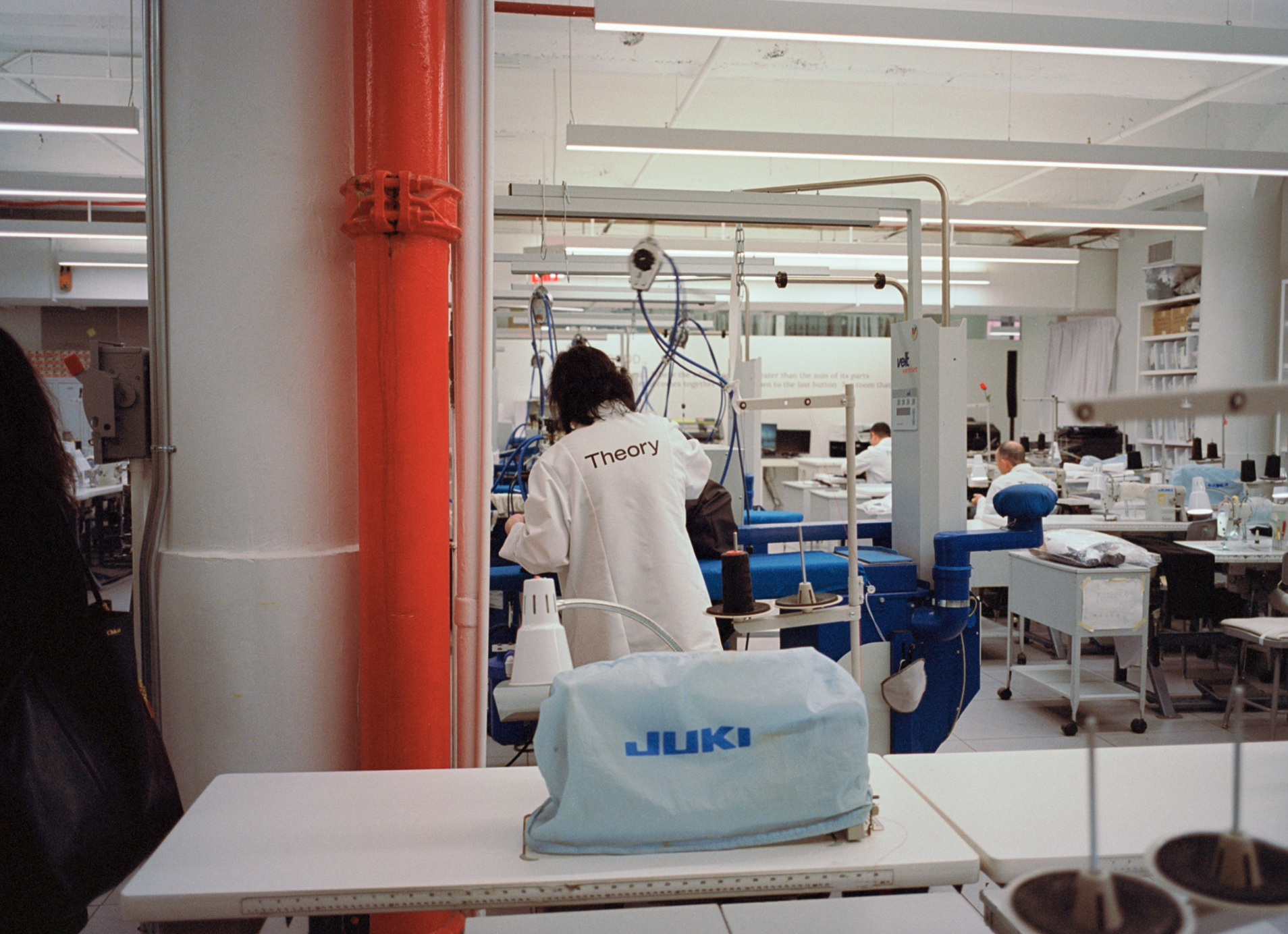 A person working in a laboratory with the word "Theory" on their white coat, surrounded by laboratory equipment and other workers.