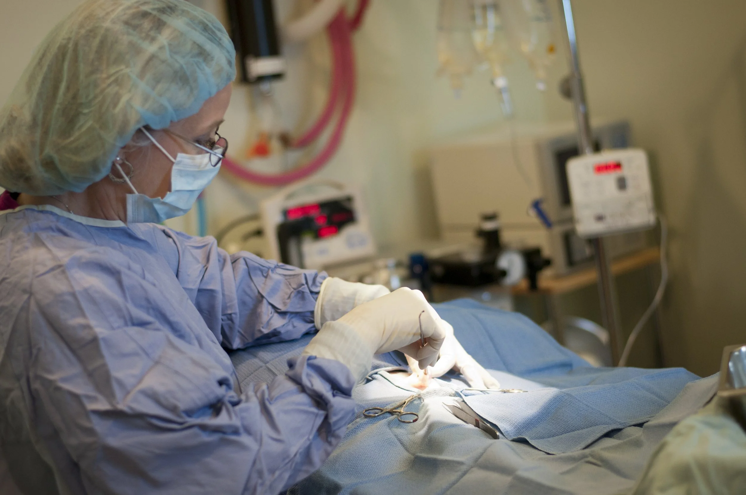 Dr. Kim in scrubs, mask, and gloves performing surgery in an operating room.