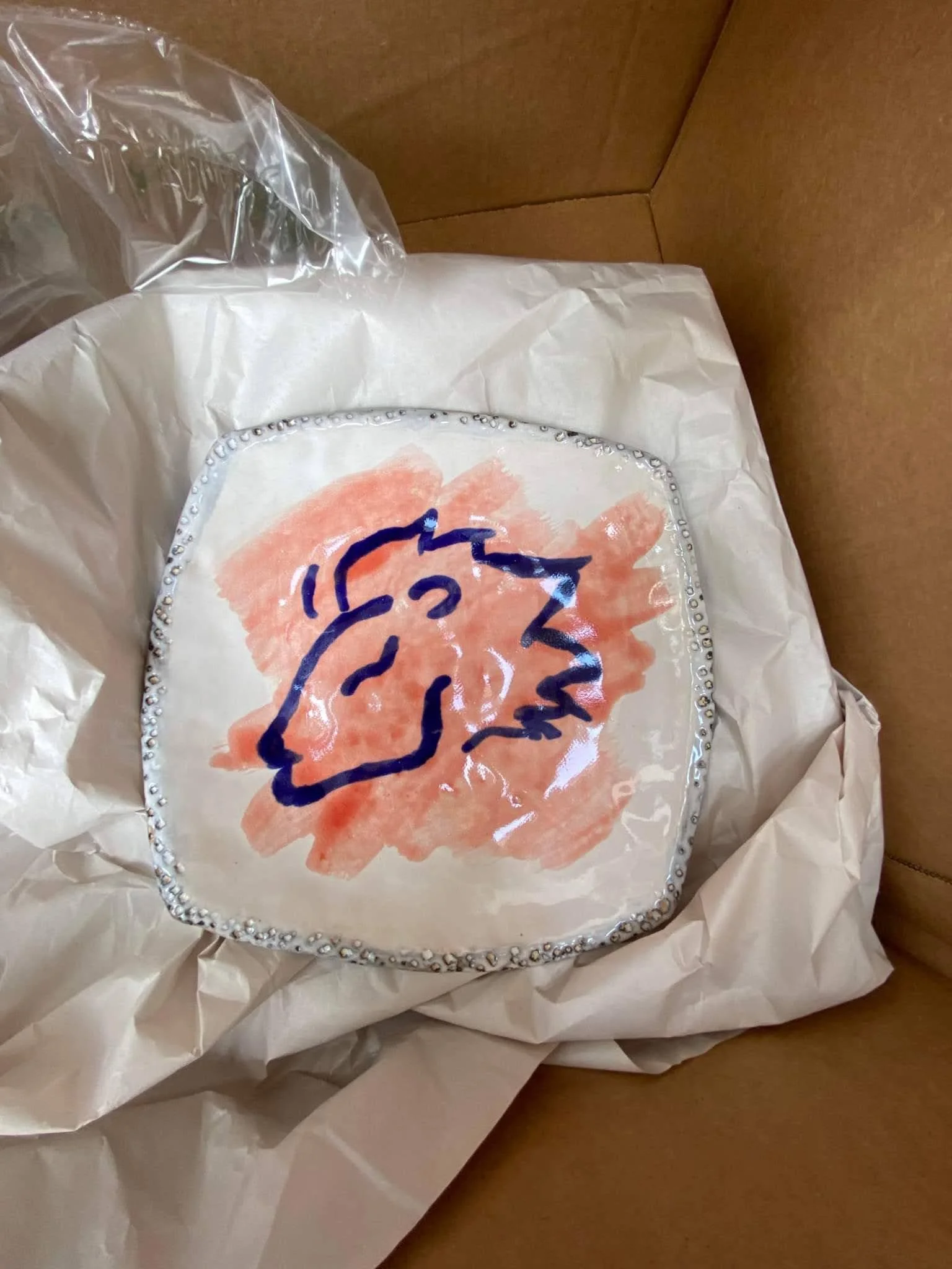 A decorated gift box with a hand-painted illustration of a unicorn on the lid, surrounded by tissue paper inside a cardboard box.