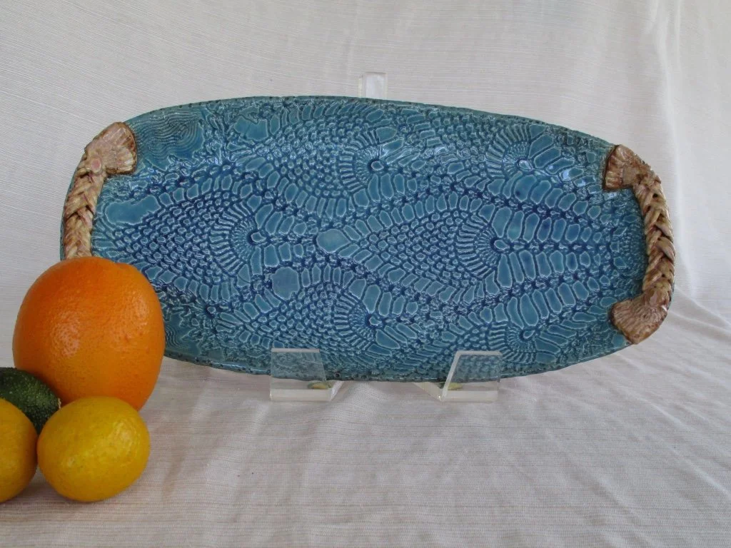 Blue decorative dish with a textured pattern, surrounded by three citrus fruits, including an orange, lemon, and lime, on a white surface.