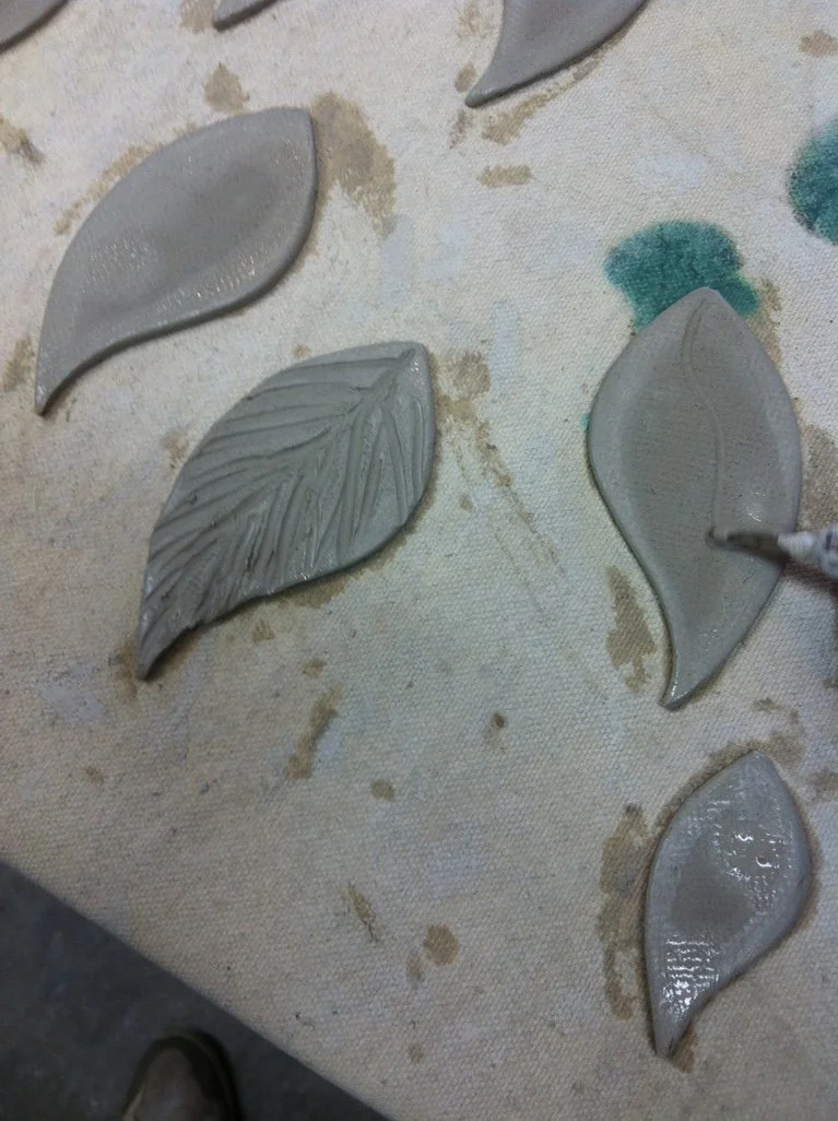 Clay or ceramic art pieces in the shape of leaves on a worktable.