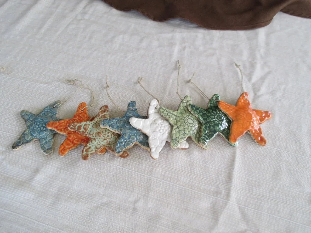 Seven star-shaped ornaments with colorful, textured patterns laid out on a light-colored fabric surface.