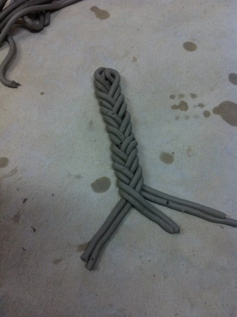 Gray electrical wires arranged in a woven pattern on a concrete floor with some stains.