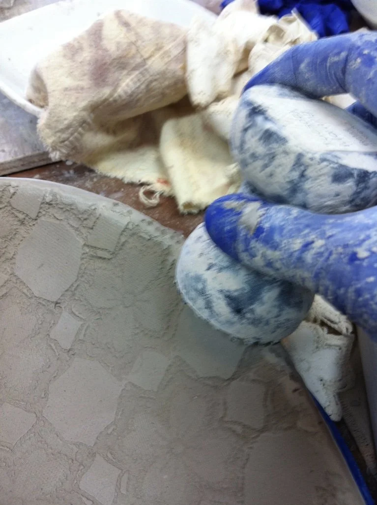 A person wearing blue gloves is applying textured plaster or stucco onto a wall with a trowel, creating a stone-like pattern.
