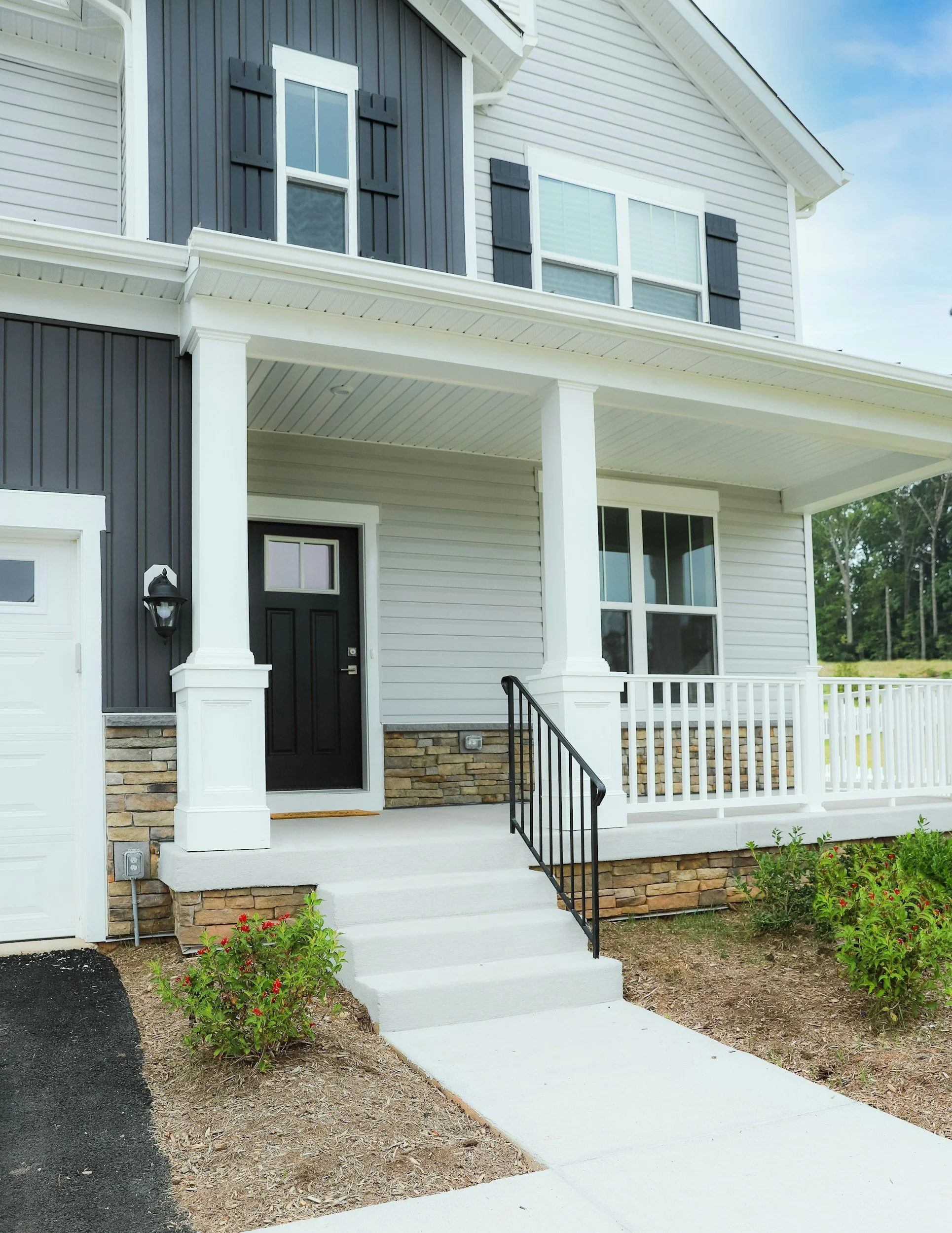 Front porch of a modern two-story house with black and white exterior, stone accents, white railing, and steps leading to black front door.