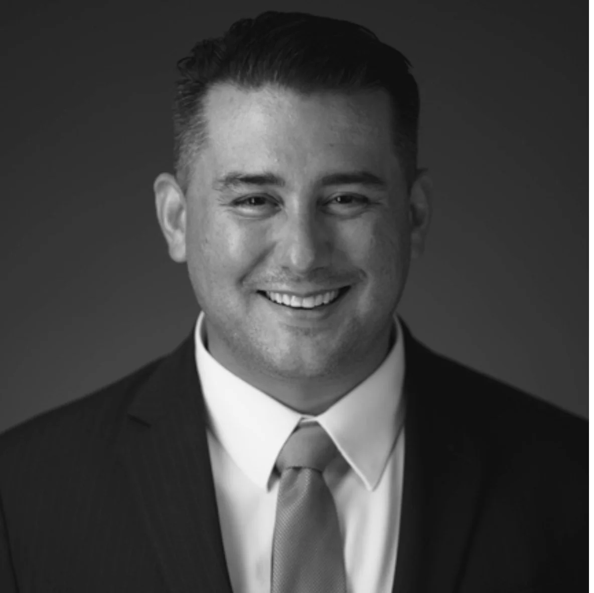 Black and white portrait of a smiling man wearing a suit, shirt, and tie.