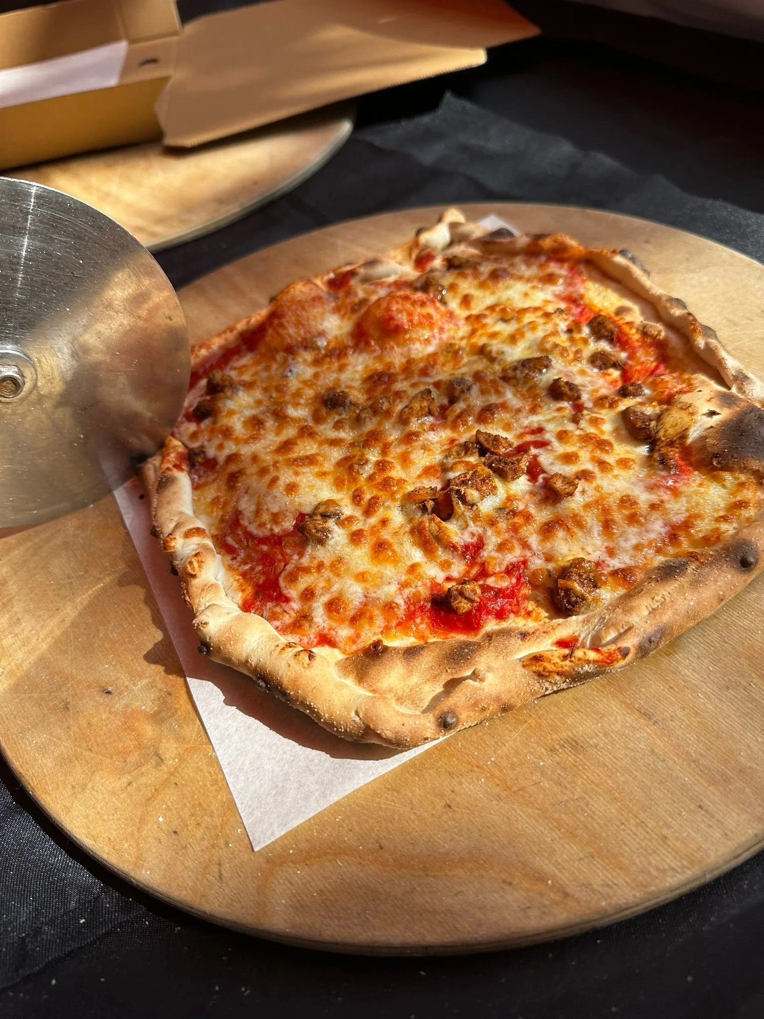 Cheese pizza with chunks of sausage on a wooden pizza board