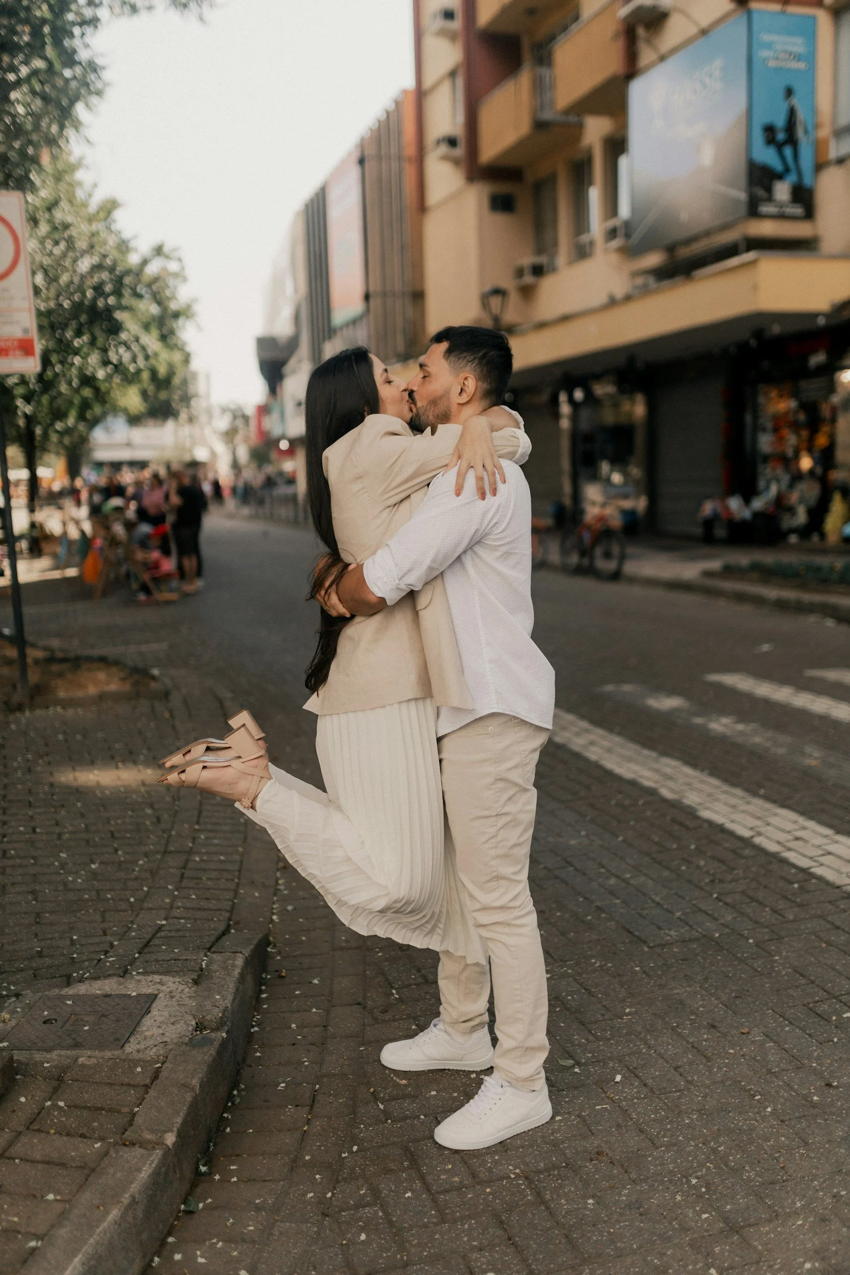 A couple embracing warmly in the middle of a street, surrounded by urban scenery.