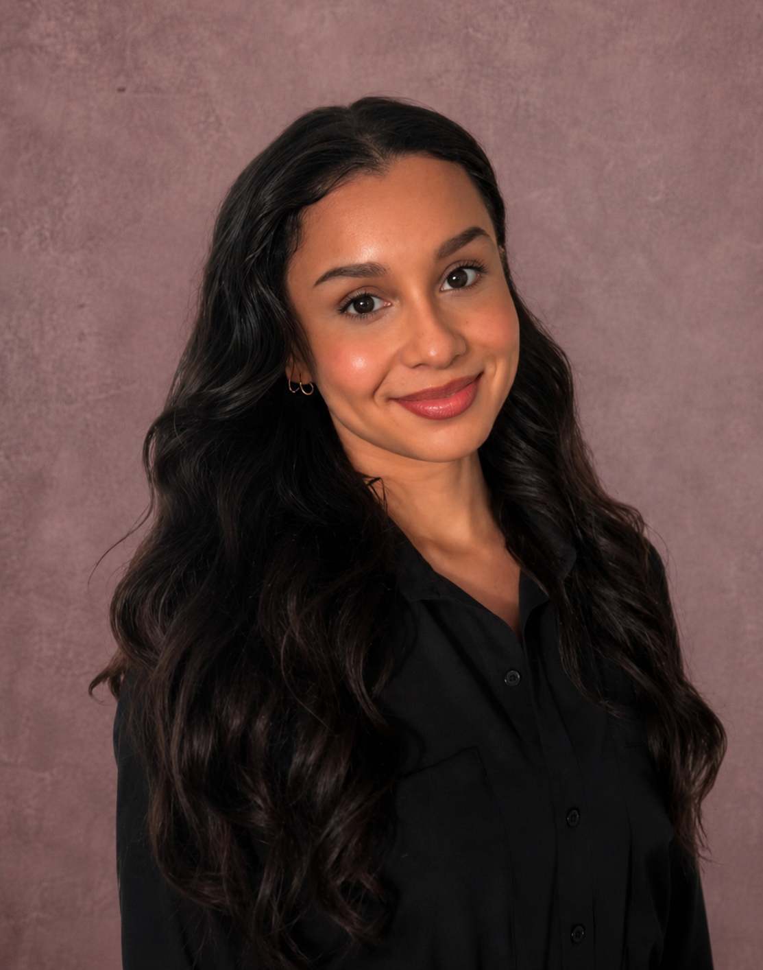 A woman with long hair wearing a black shirt, standing confidently with a neutral expression.