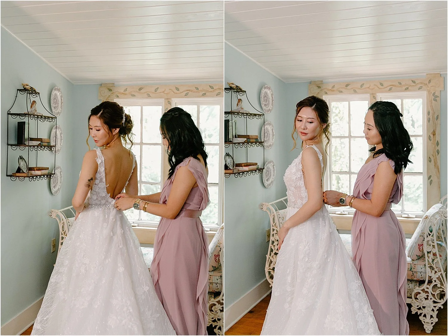 A bride in a wedding gown is being helped with her dress by a woman in a mauve dress in a bright room with windows and decorative plate wall hangings.
