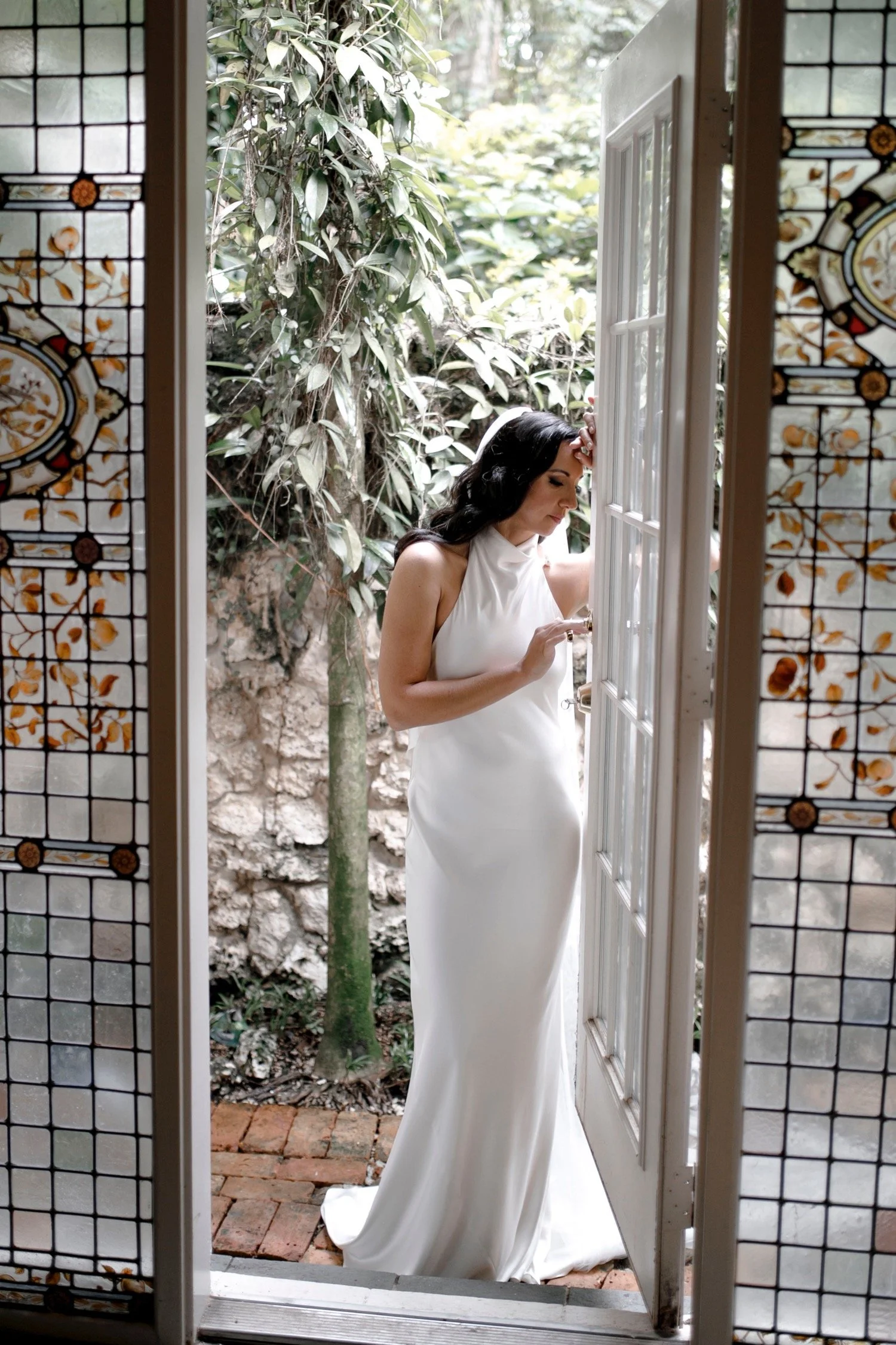 Woman in a white dress standing in a doorway, surrounded by greenery.