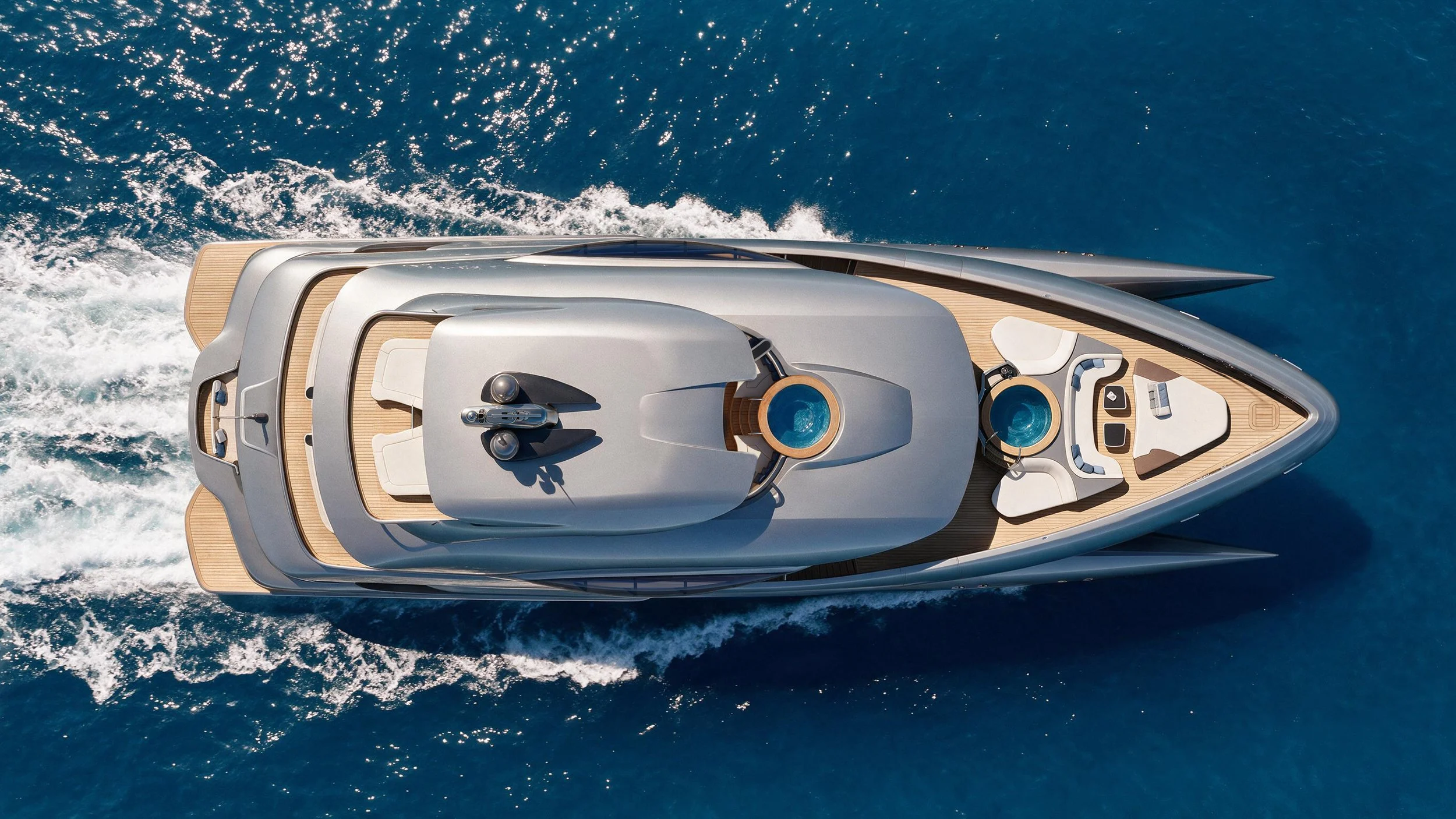 Top view of a wavepiercer superyacht with two spas on the deck and lounge seating, going through the ocea