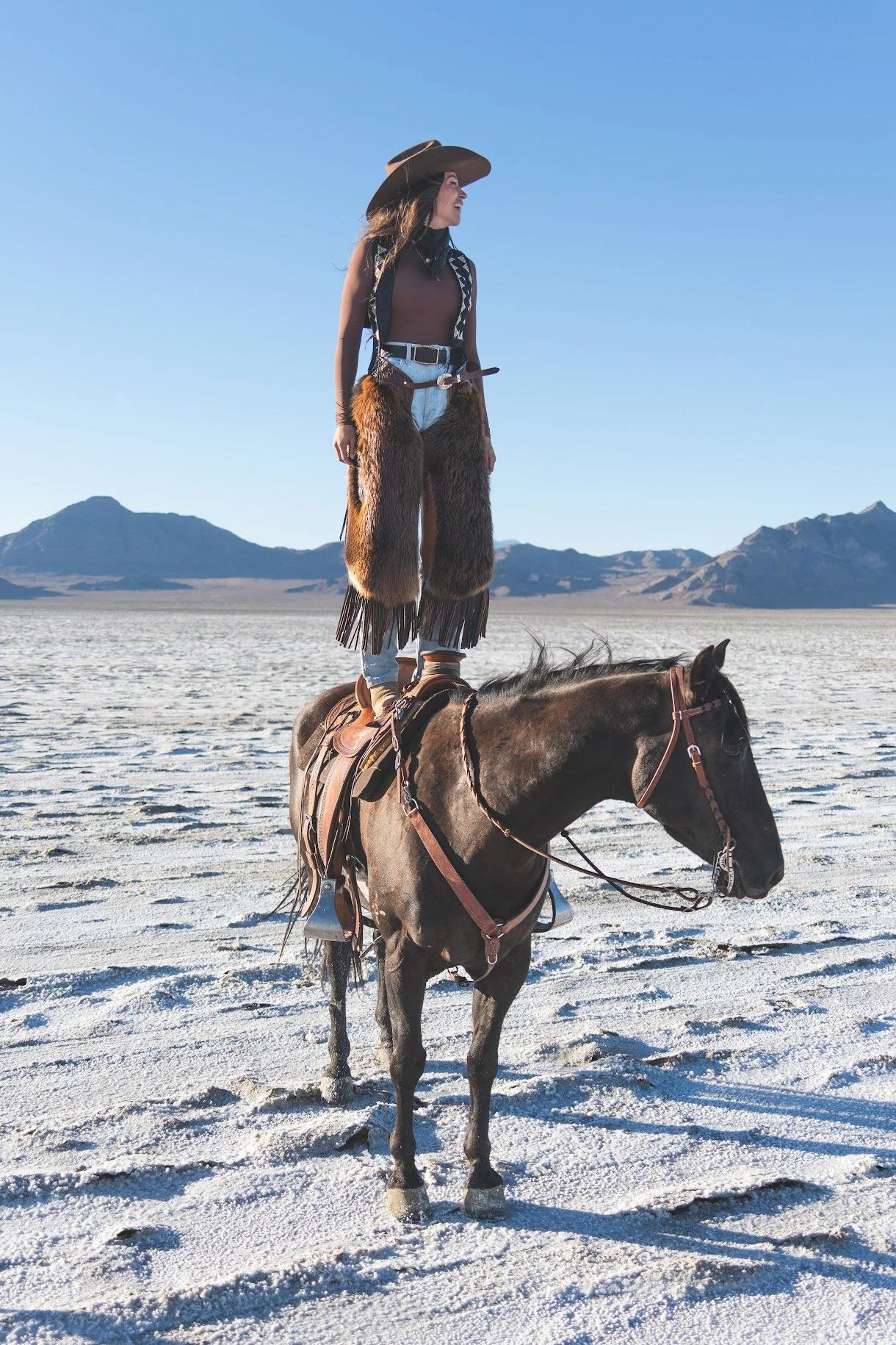 Cowgirl Standing on Horse | Western Editorial at Salt Flats- Cowgirl standing tall on horseback at the Bonneville Salt Flats wearing wide-brim hat, chaps, and boots. Western lookbook photo symbolizing strength, balance, and frontier style.