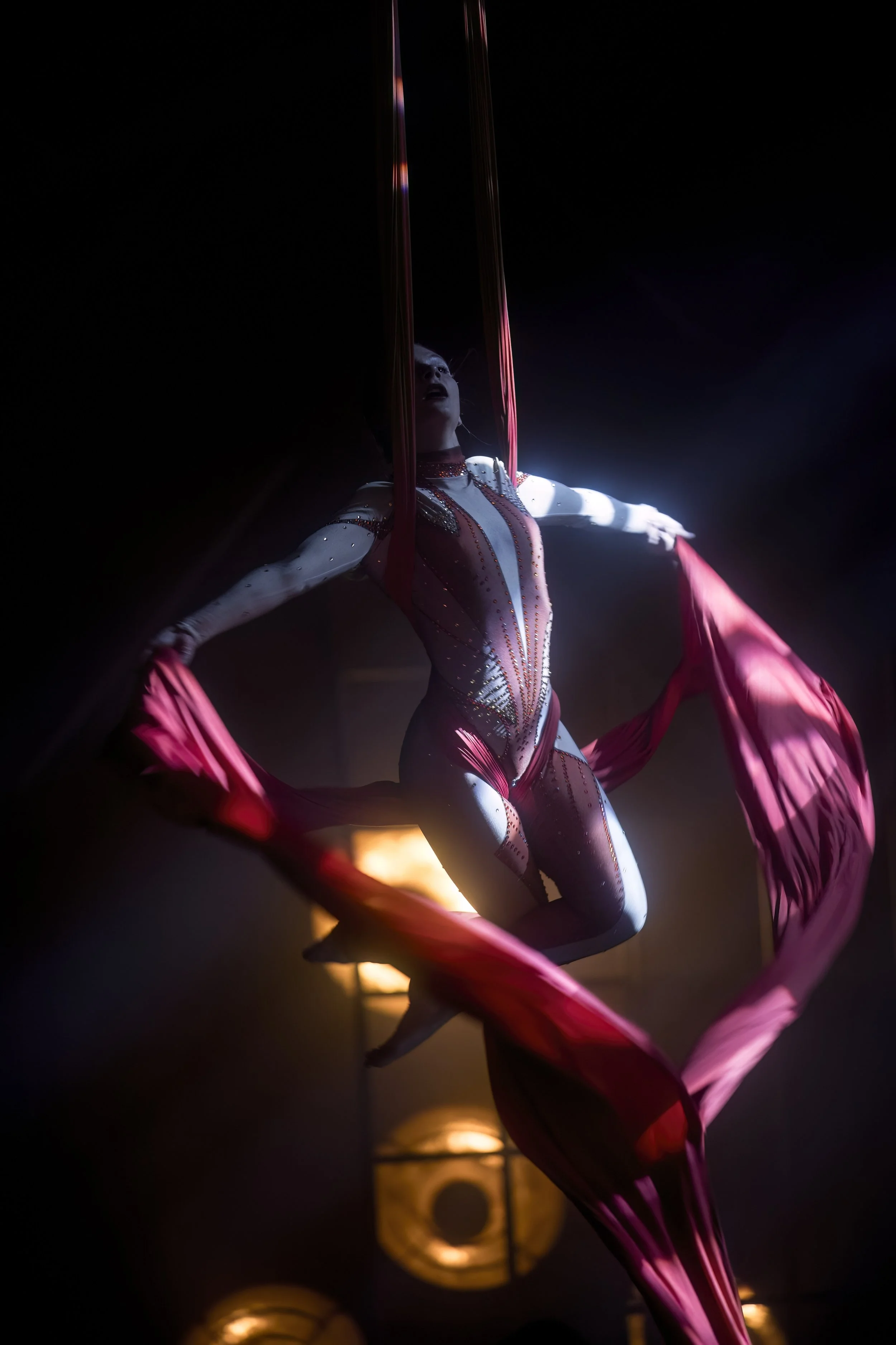 Ivy Kolcun in a dynamic aerial silk pose surrounded by deep red and blue stage light during Blue Secret Show