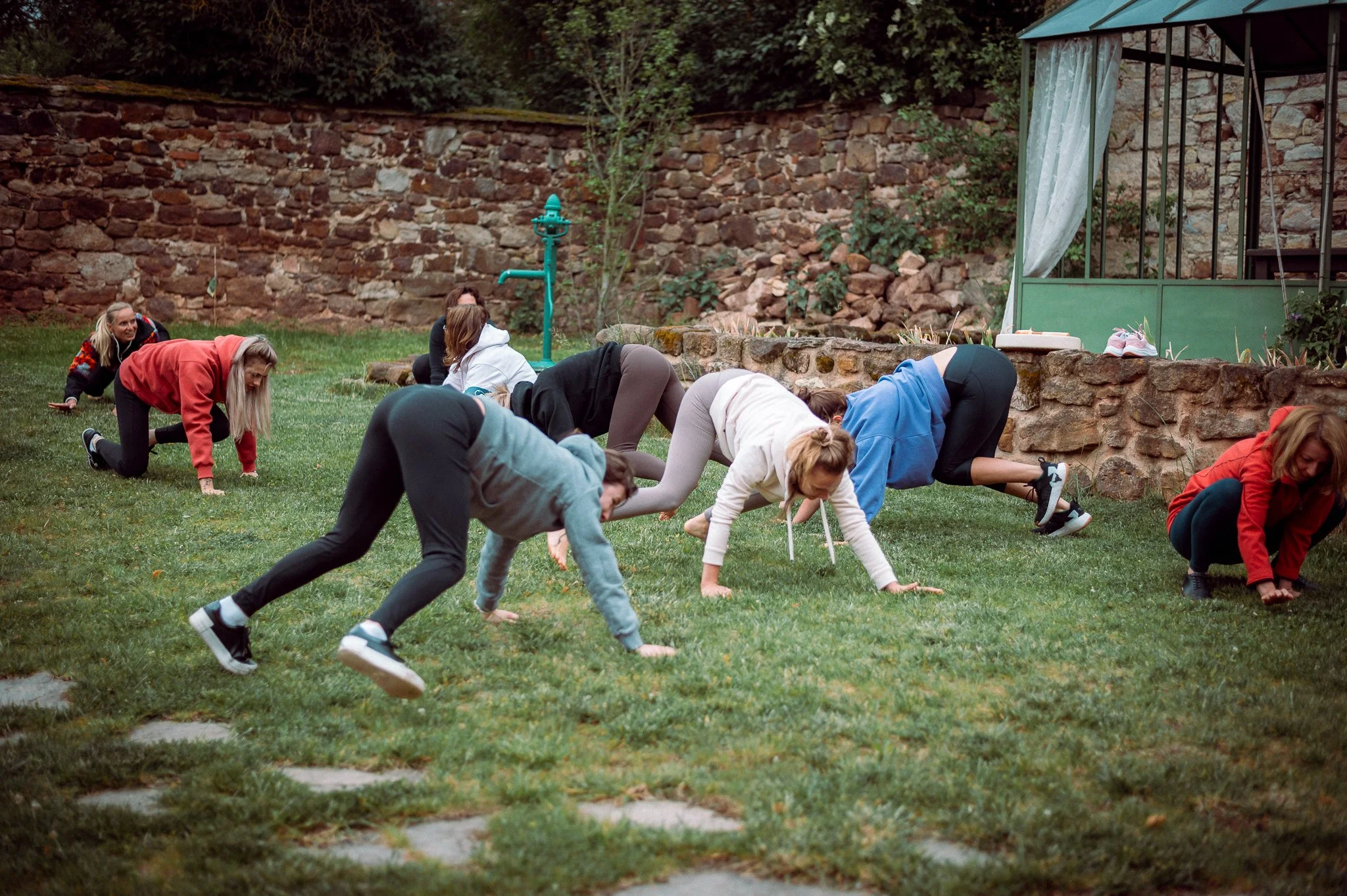 A group of people exercising outdoors on a grassy area, performing a plank or crawling exercise together.
