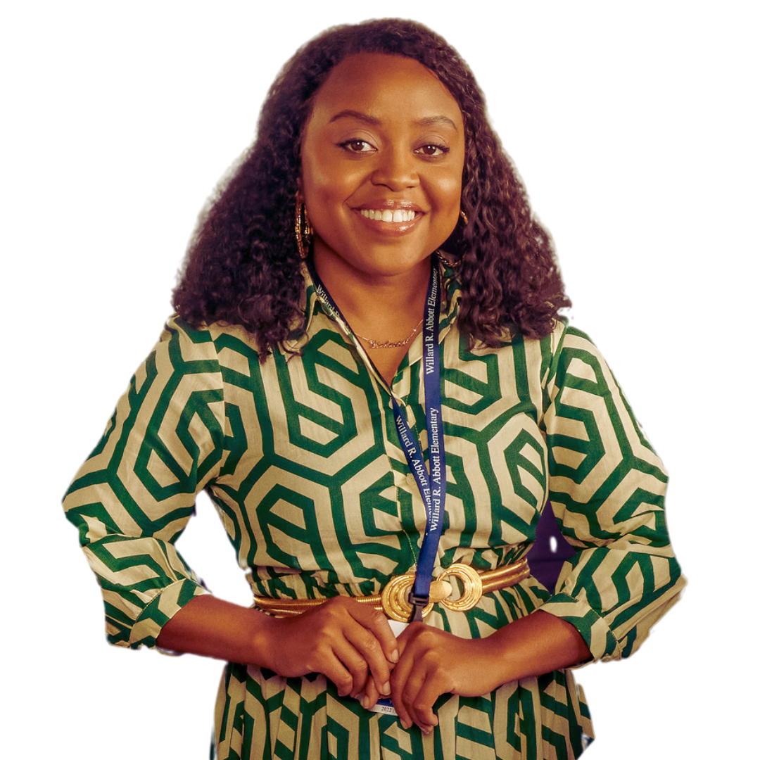 Janine Teauges from Abbott Elementary wearing a green and beige patterned blouse with a gold belt, smiling, with a blue lanyard around her neck at an indoor event.