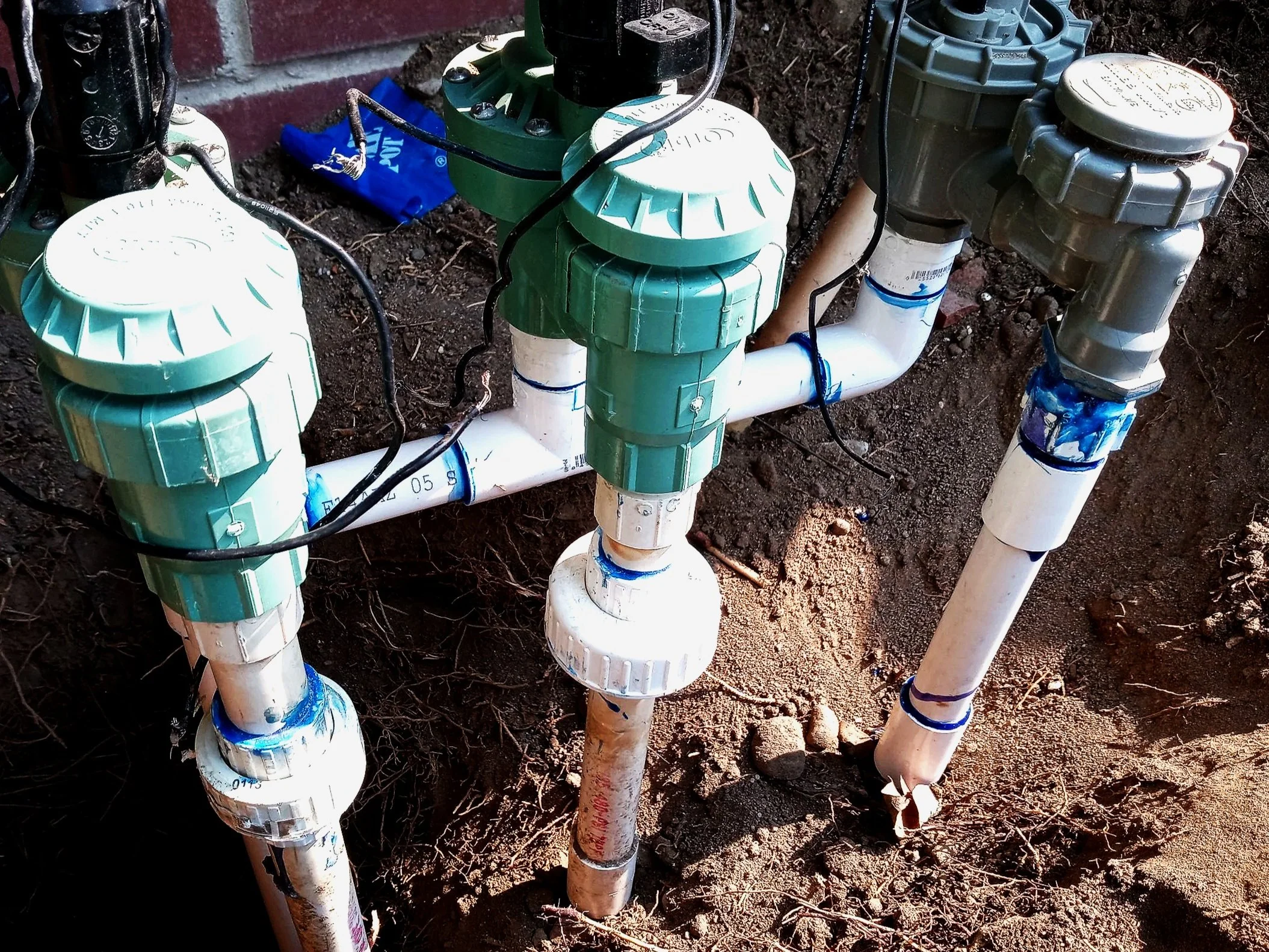 A plumbing system with white PVC pipes and green and grey water valves installed underground in soil for irrigation or water management.