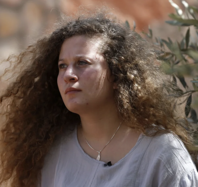 A middle-aged man with light brown hair and blue eyes, smiling. He is wearing a dark blazer over a light blue collared shirt, against a gray background.