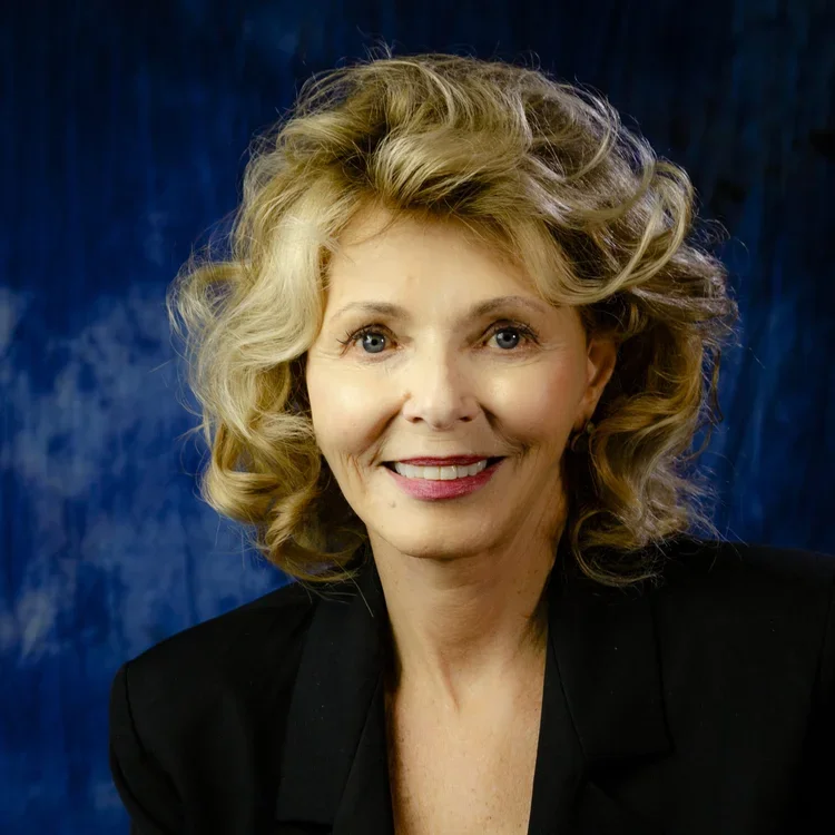 A portrait of a young man with short dark hair, wearing a black collared shirt, smiling against a dark background.