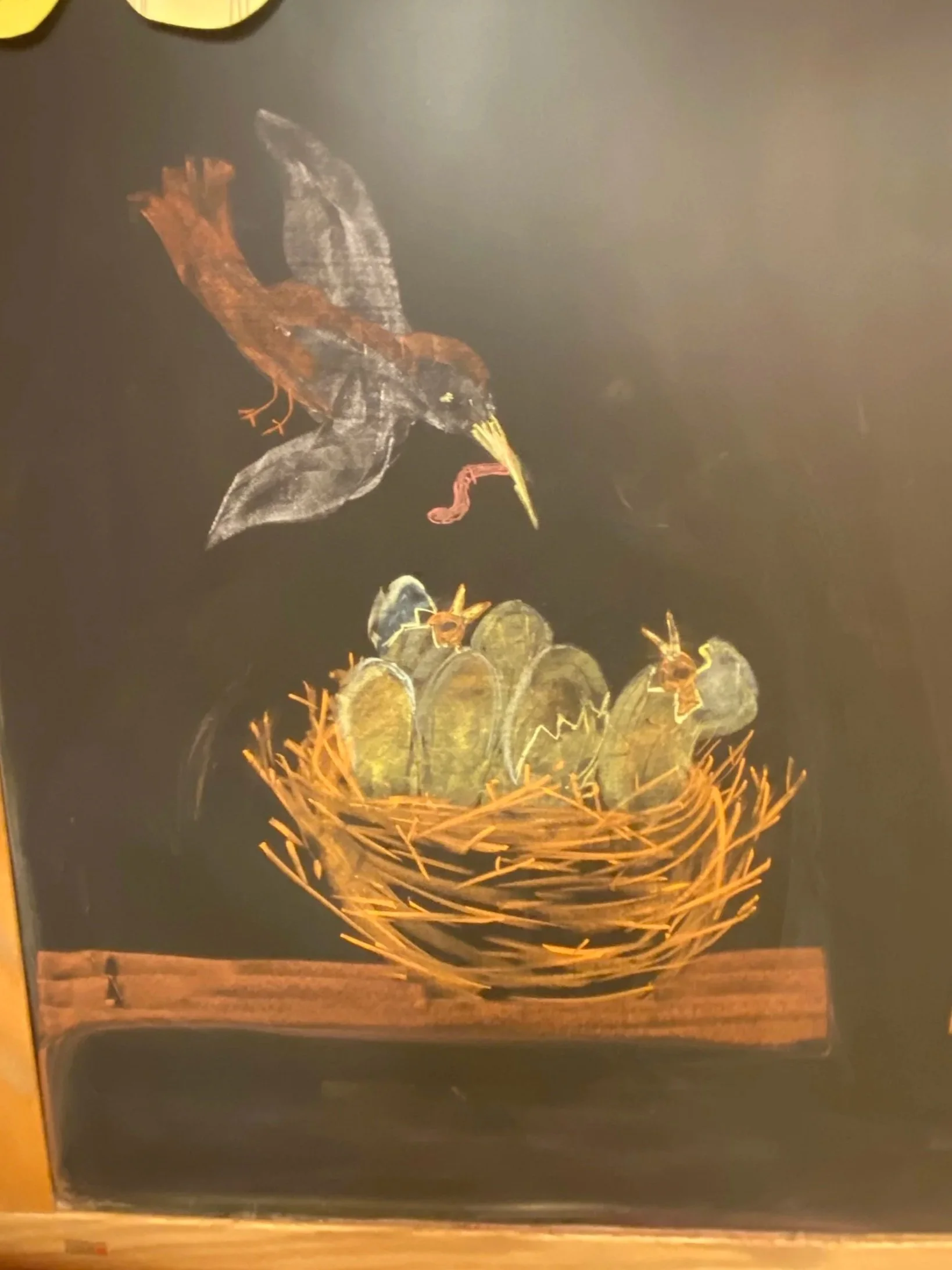 Chalk art depicting a bird, possibly a heron, flying over a nest with cacti and birds on a black background.