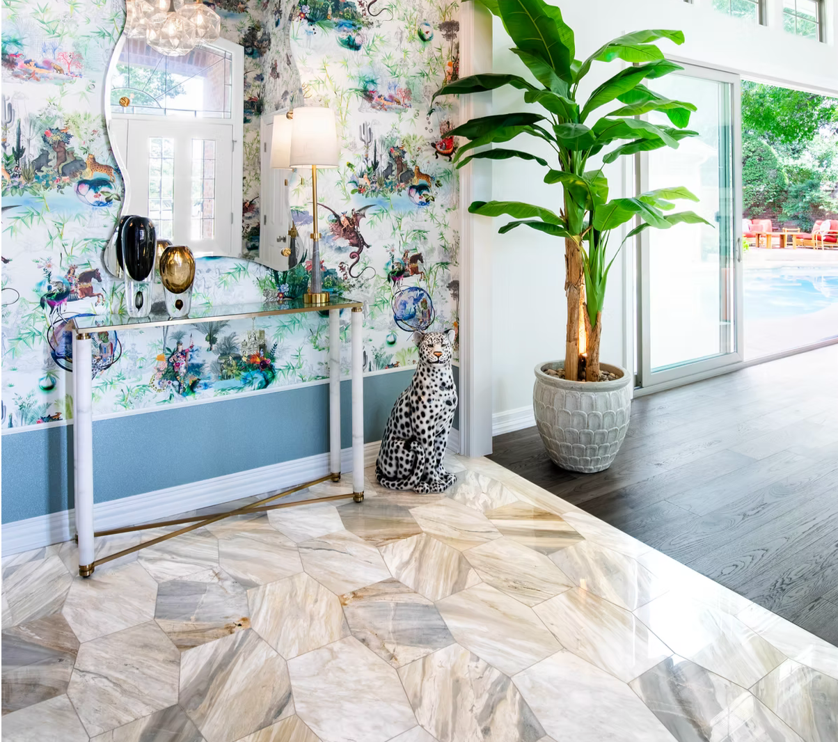 Interior of a bright, modern home featuring a marble floor, a large potted banana plant, and a decorative leopard sculpture. The space has a colorful wallpaper with a jungle theme and a glass sliding door leading outside to a pool area.