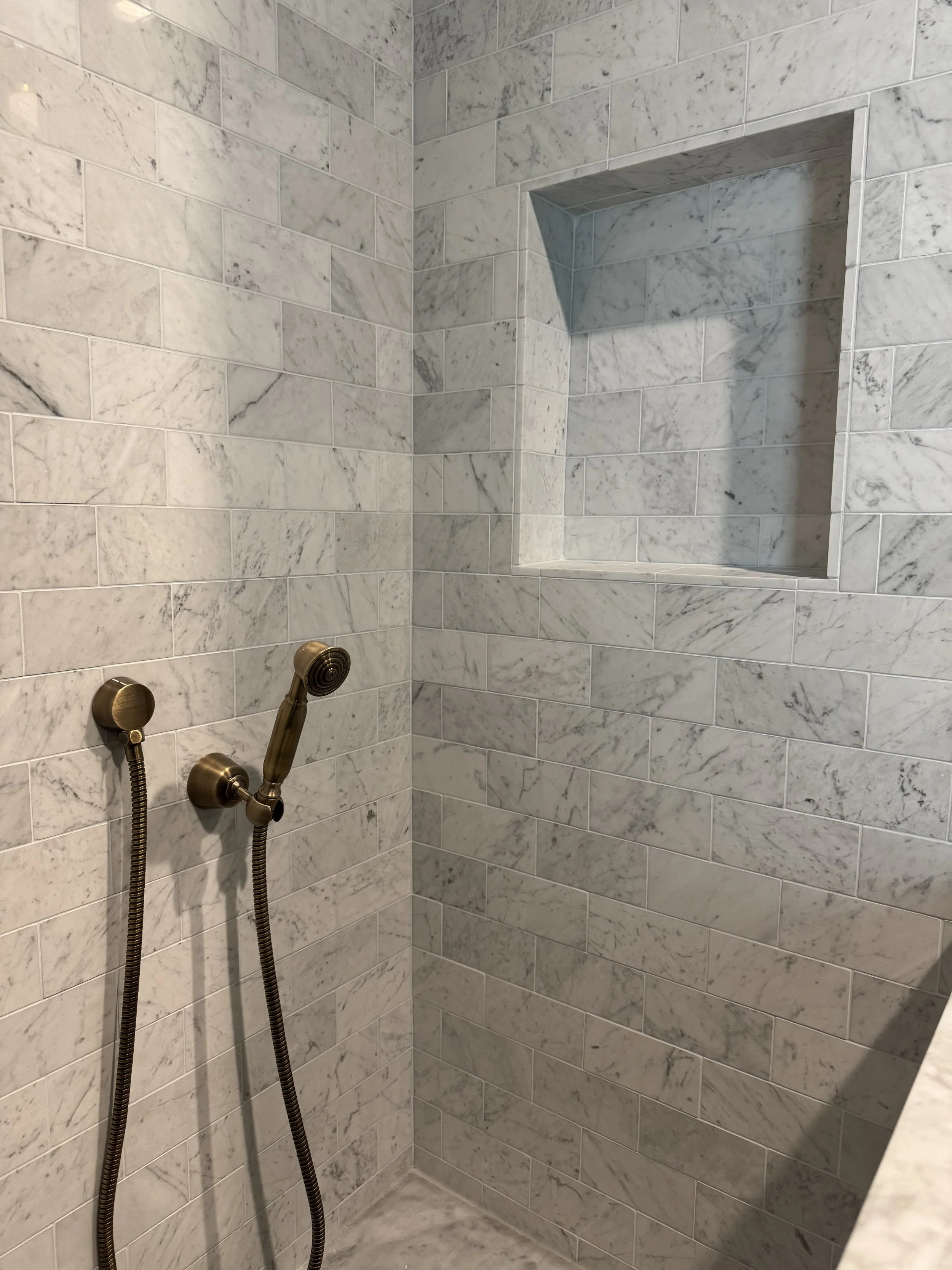 A marble shower with built-in niche and brushed bronze handheld showerhead.