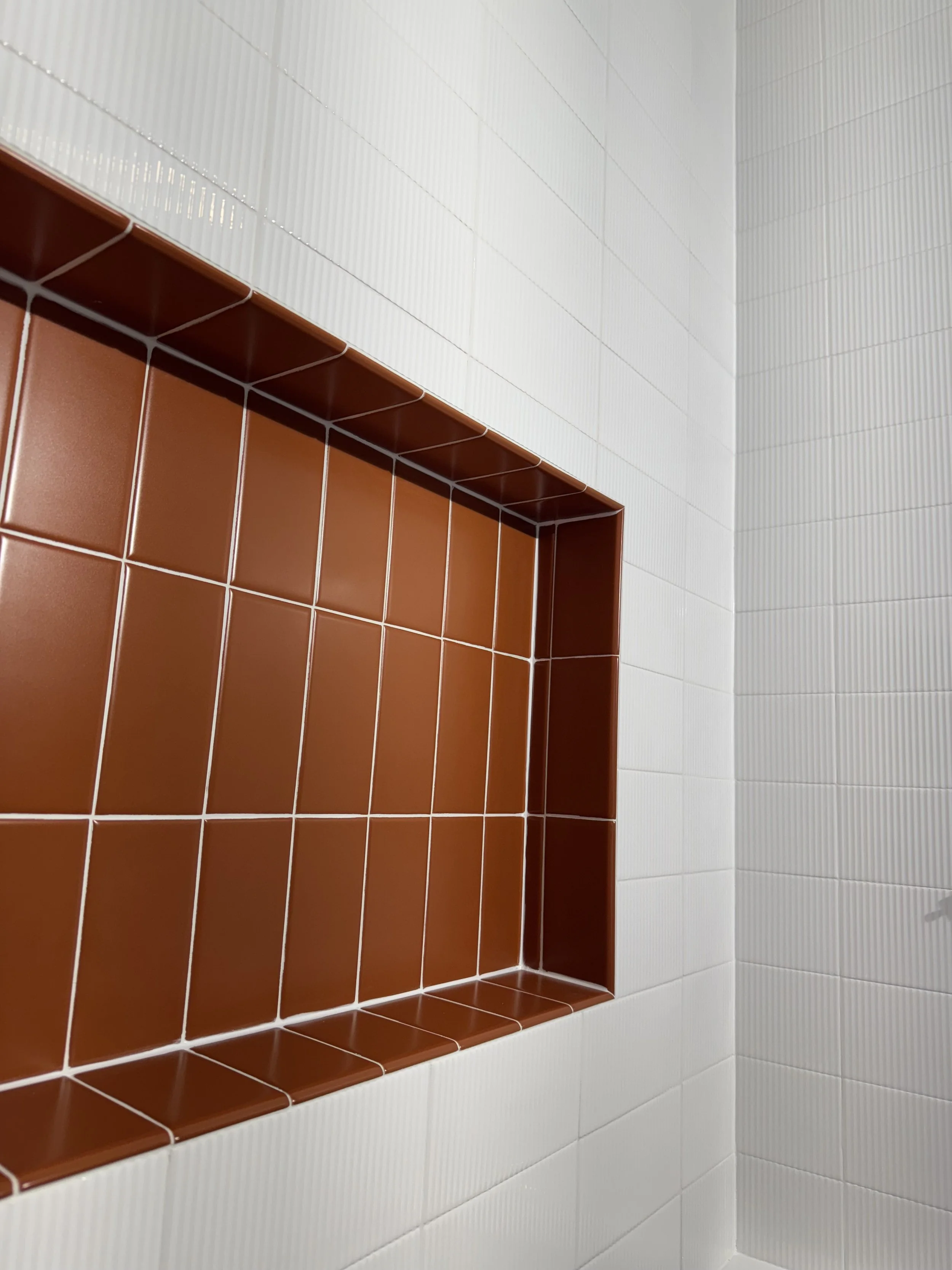 A shower niche with brown tiles, surrounded by white tiled walls.