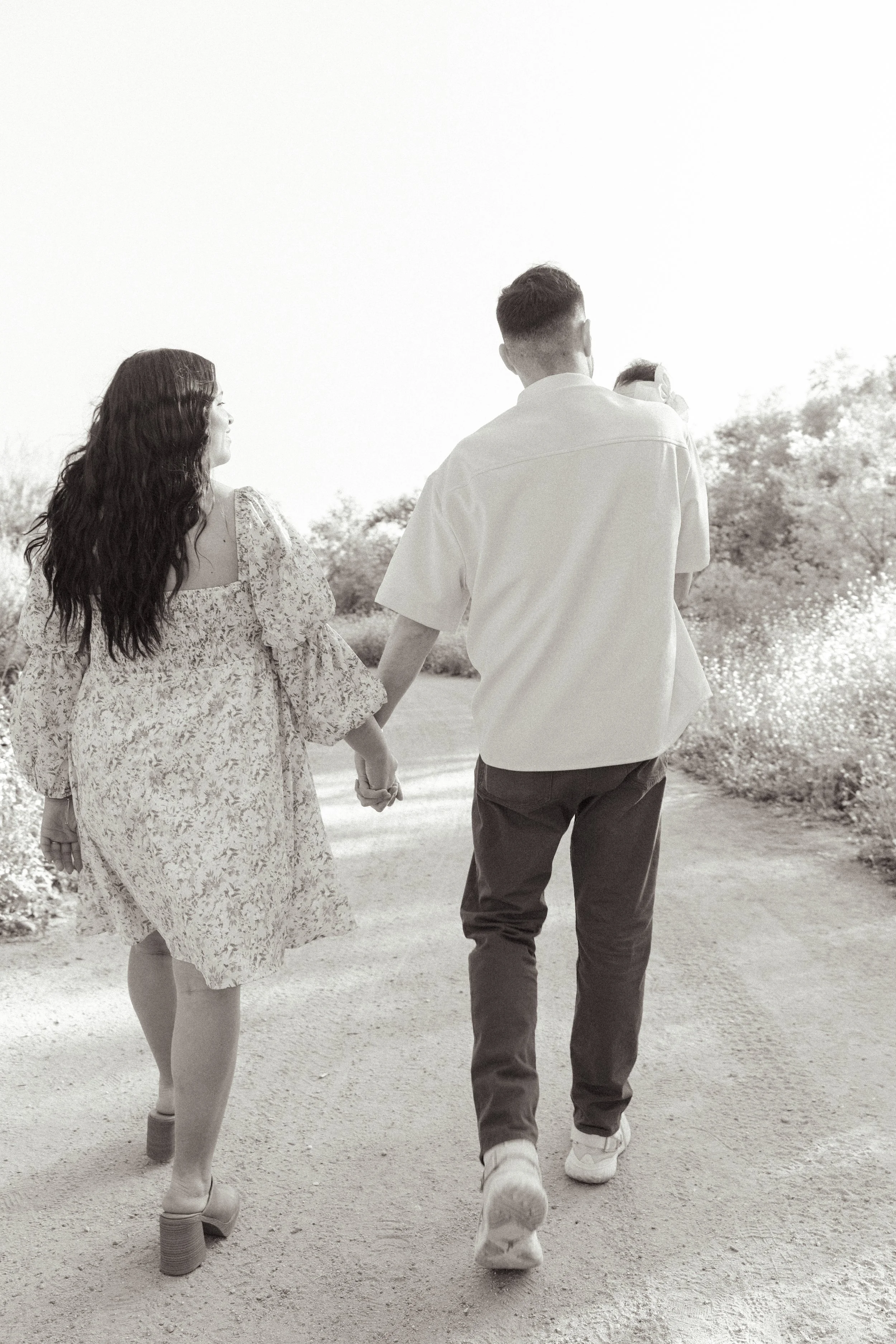 A black-and-white photo of a couple holding hands as they walk down a dirt path through a park or garden. Family portraits Corona California (Local Photographer)