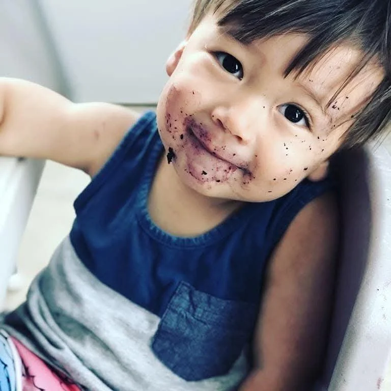 A young boy with a messy face covered in chocolate smudges and crumbs, smiling at the camera.