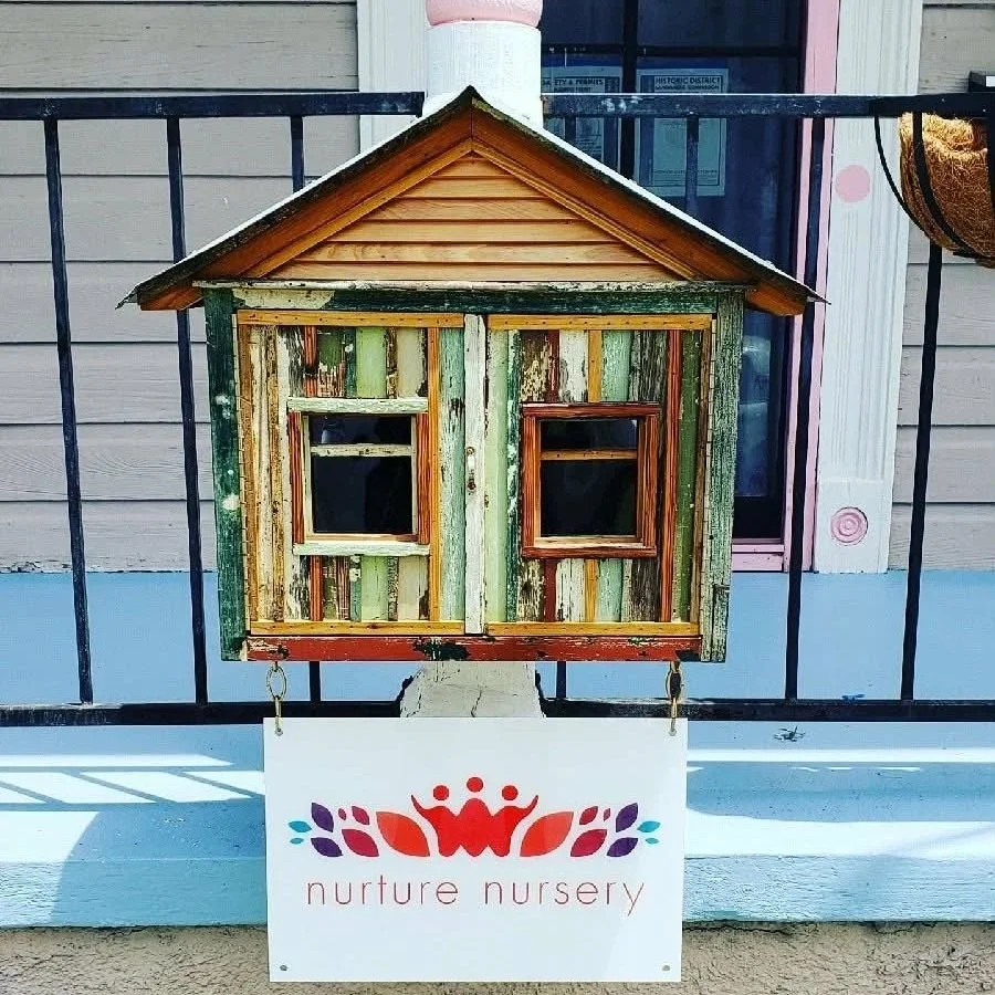A small decorative wooden house structure mounted on a black metal fence, labeled "nurture nursery."