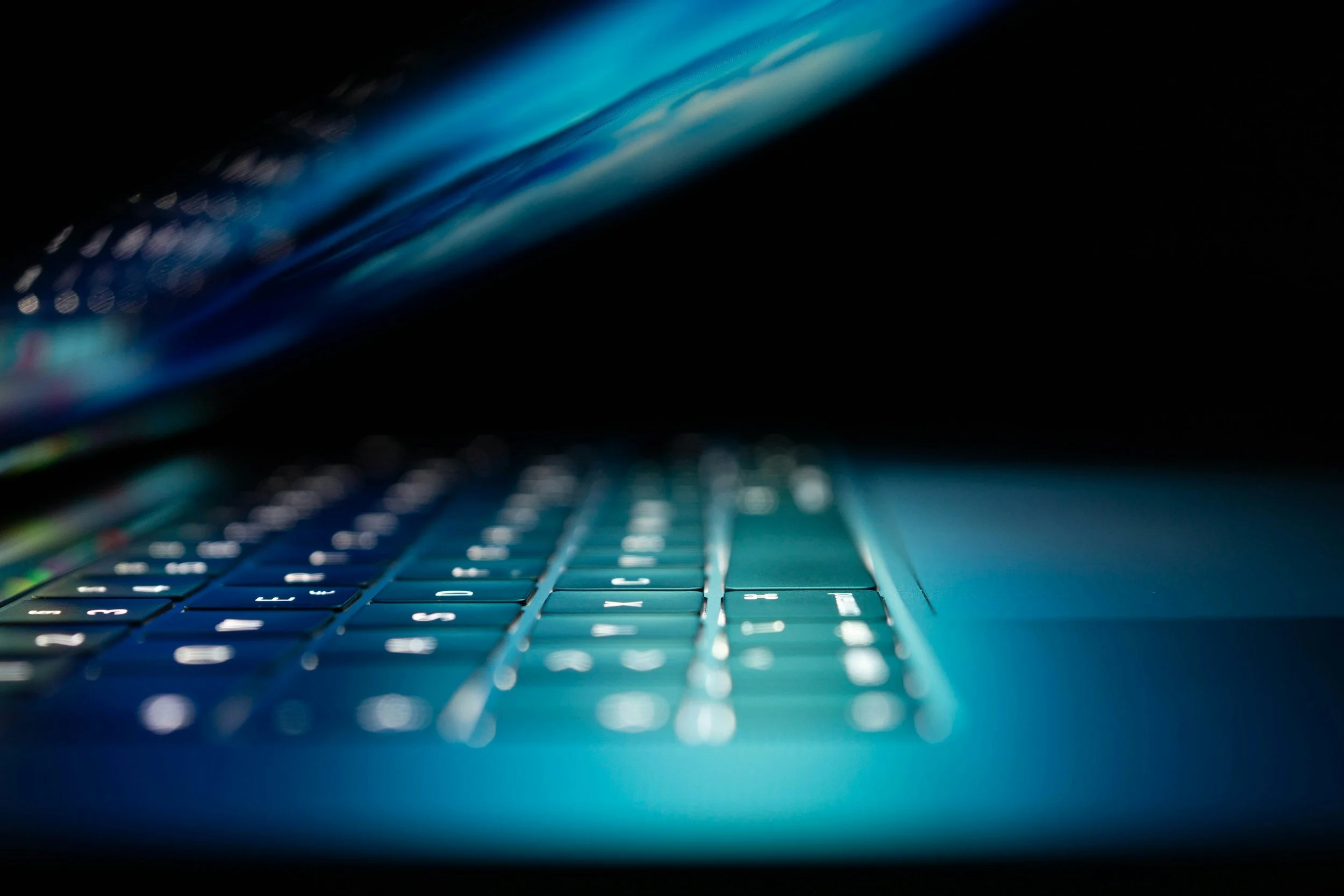 Close-up of a computer keyboard with illuminated keys, taken from a low angle in a dark environment.