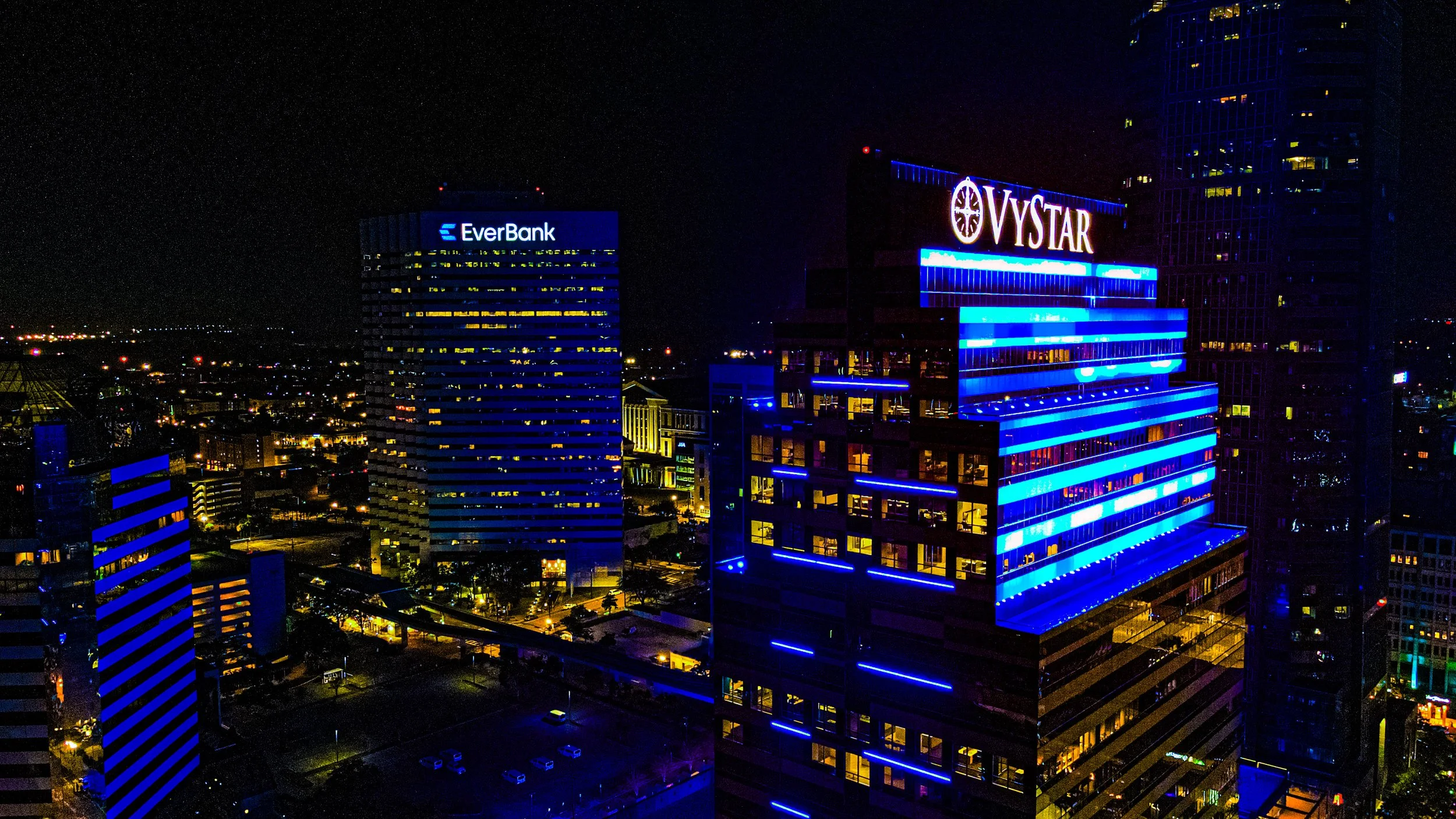 Nighttime cityscape with illuminated skyscrapers, featuring blue lighting and visible signage for EverBank and Vystar.
