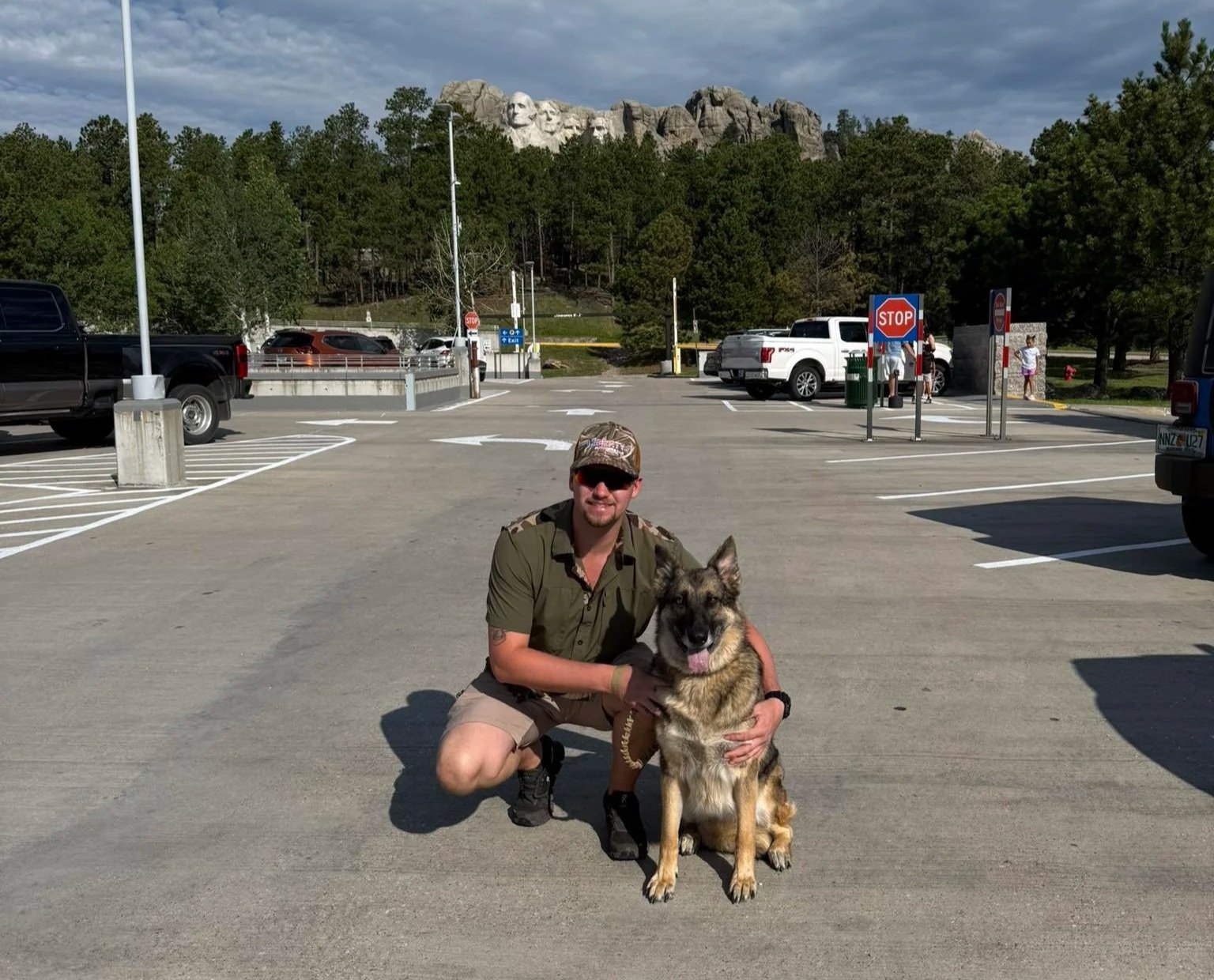 Hunter Meeks crouching next to his German Shepherd dog in a parking lot with Mount Rushmore in the background.