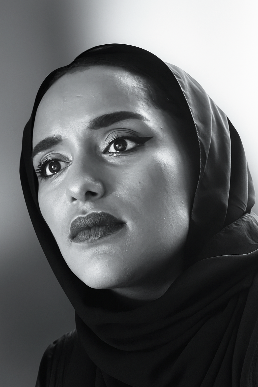 Close-up black and white portrait of a woman wearing a headscarf, with detailed facial features and expressive eyes.