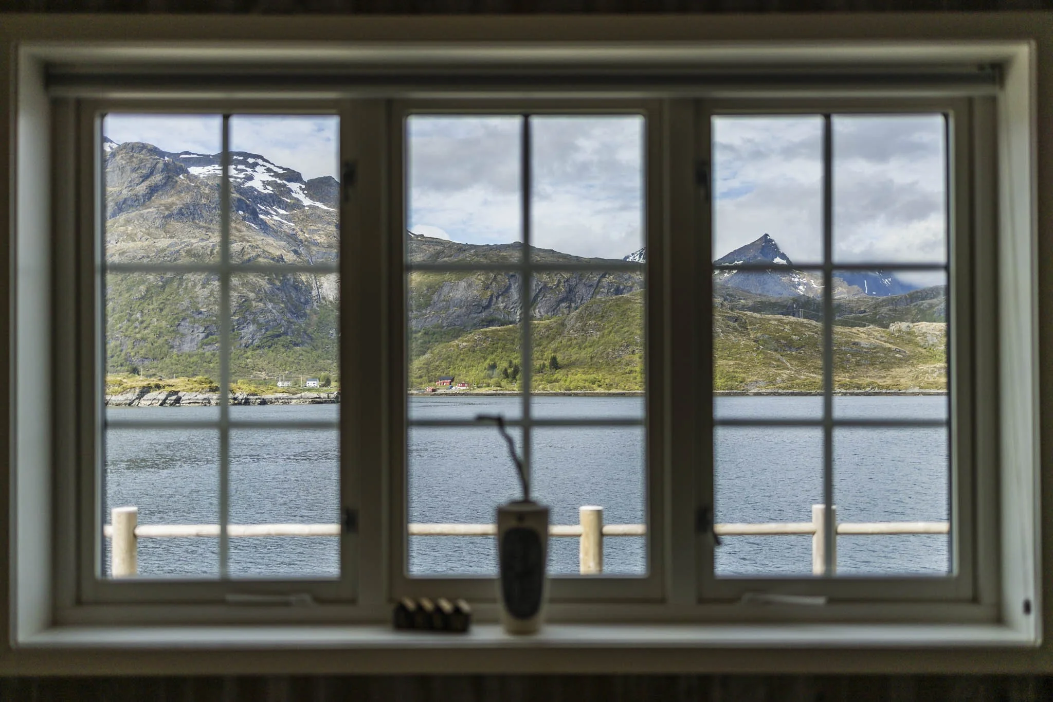 View of snow-capped mountains and a body of water through a window with grid panes.