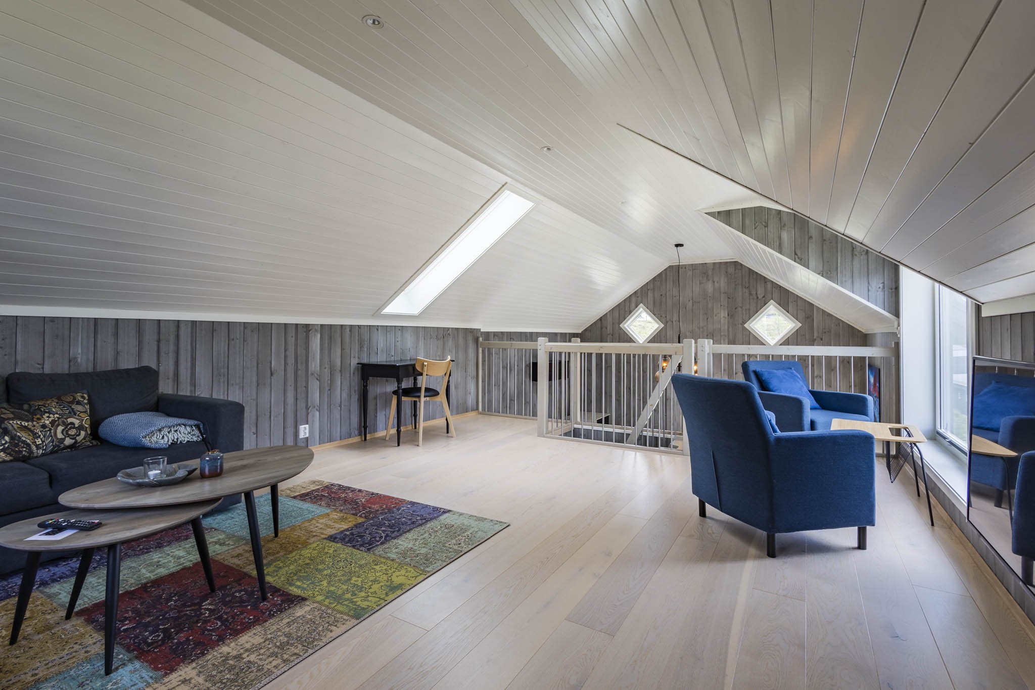 Living room with a gray couch, colorful rug, wooden coffee table, blue armchairs, and a gray-paneled wall.