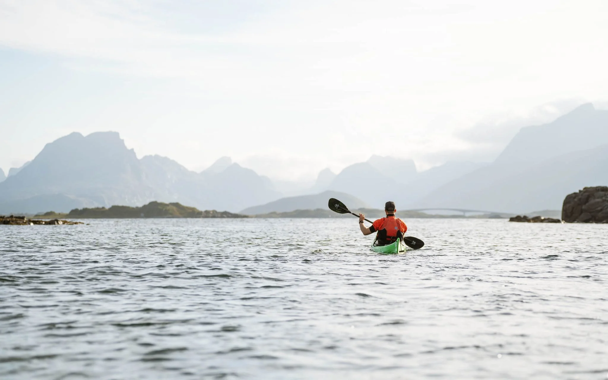 Person kayaking on a body of water with mountains in the background.