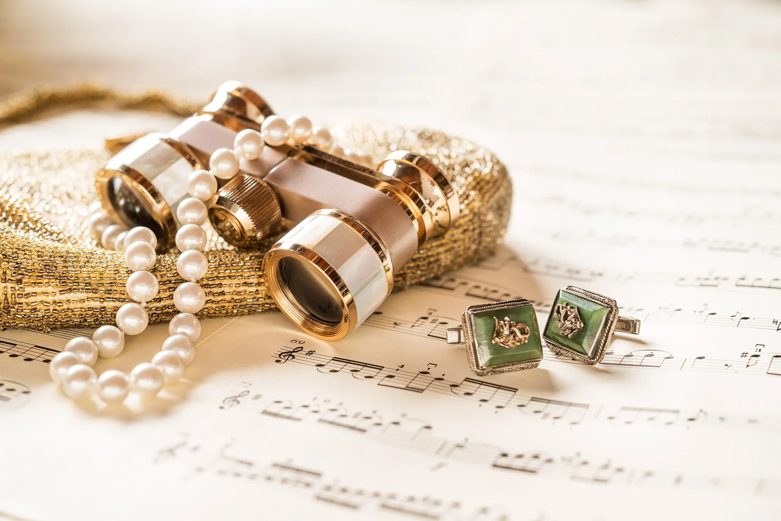 Jewelry including a pearl necklace, gold bracelet, and cufflinks, along with a vintage perfume bottle, all arranged on sheet music.