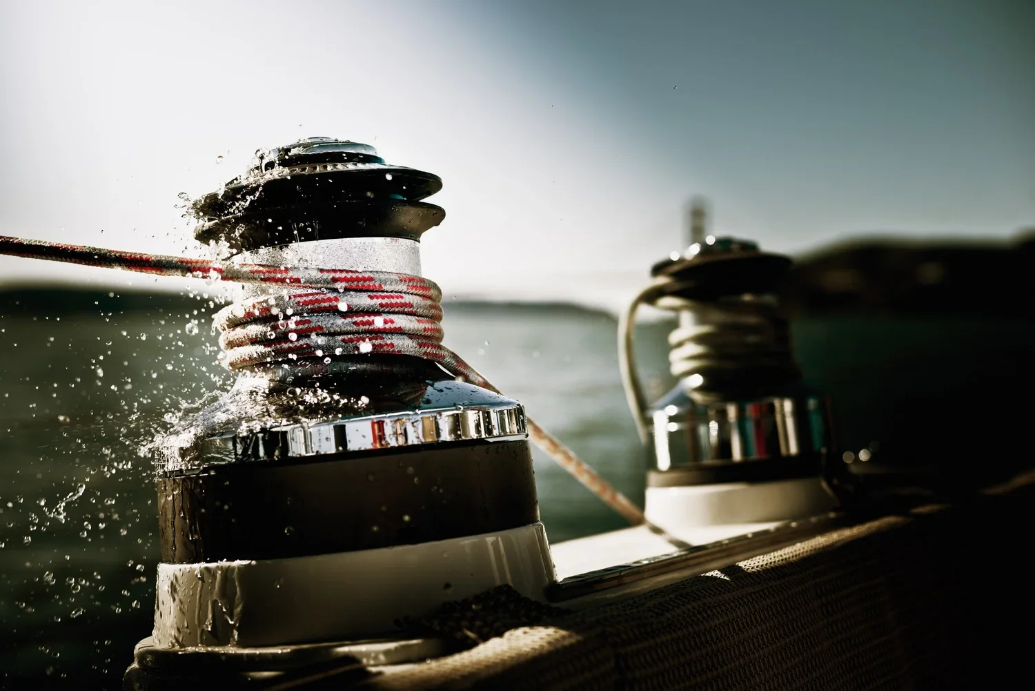 Close-up of boat winches with ropes, water splashing, on a boat with a body of water in the background.