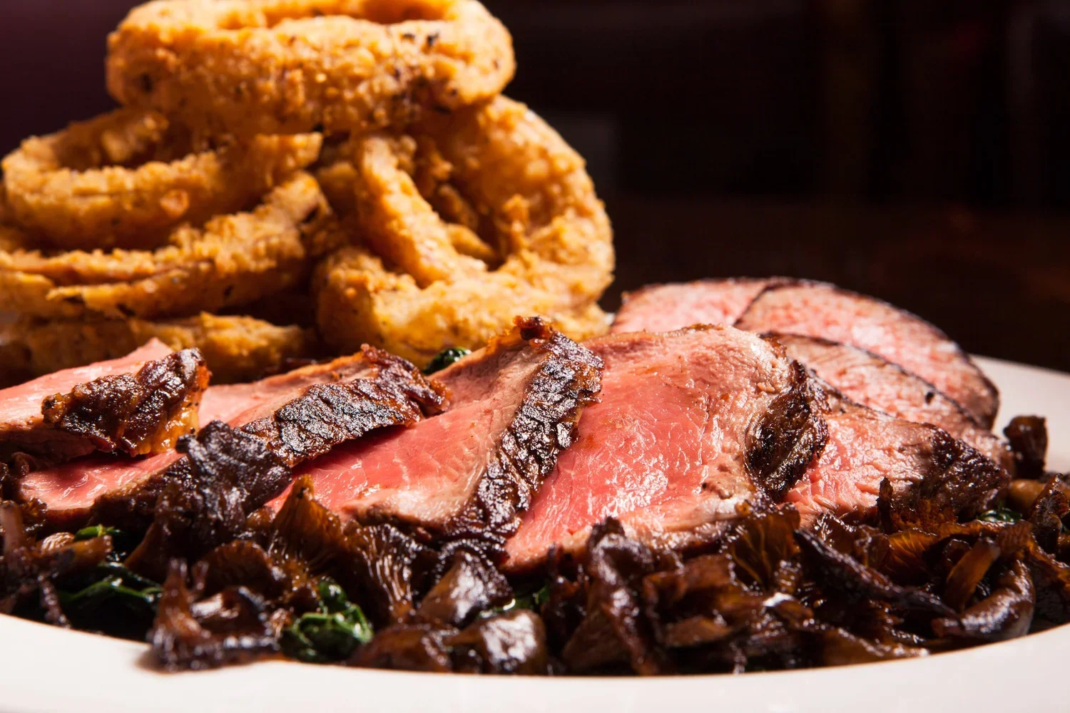 A plate of sliced beef tenderloin with a dark sauce on top, served with fried onion rings and caramelized onions.