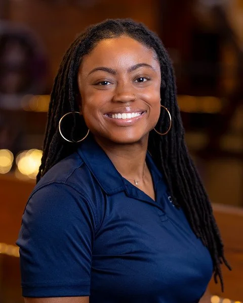 Close-up of a young African American woman with dreadlocks, smiling, wearing hoop earrings and a nose ring.
