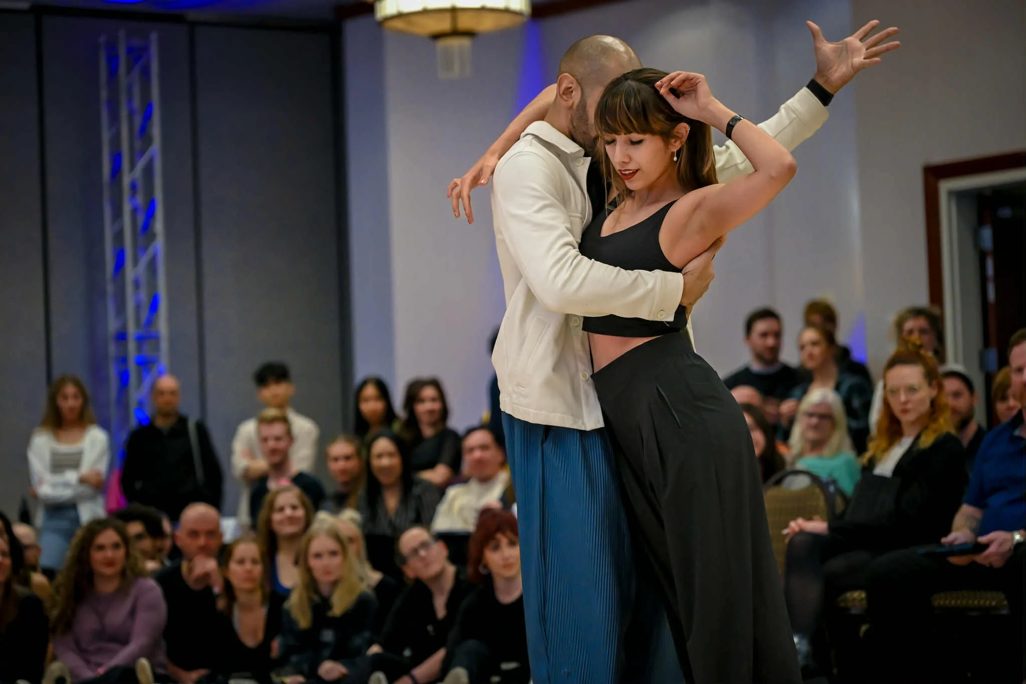 A man and a woman dancing closely in front of an audience at an indoor event.
