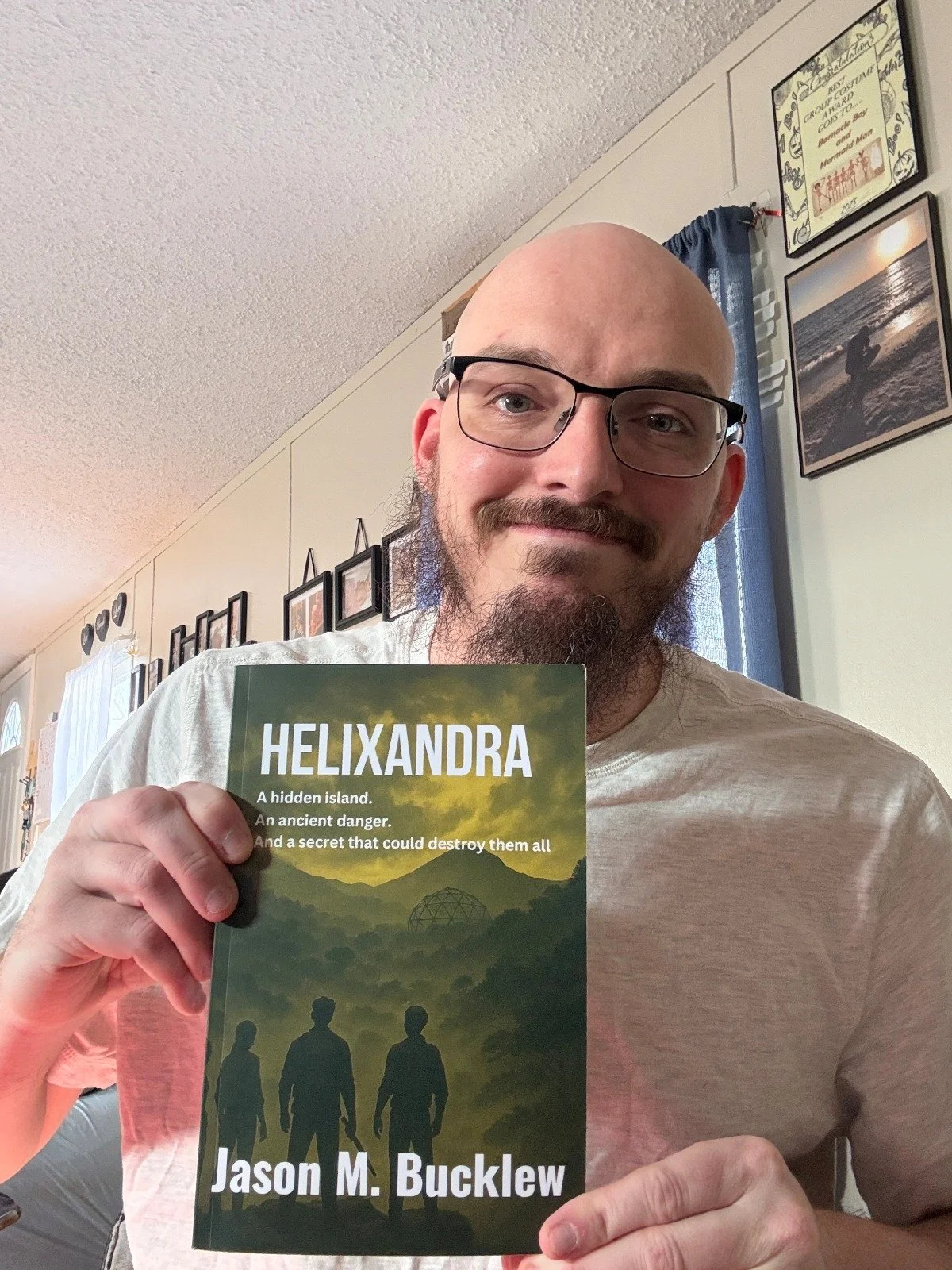 Author Jason M. Bucklew smiling and holding a paperback copy of his survival science fiction novel, Helixandra.