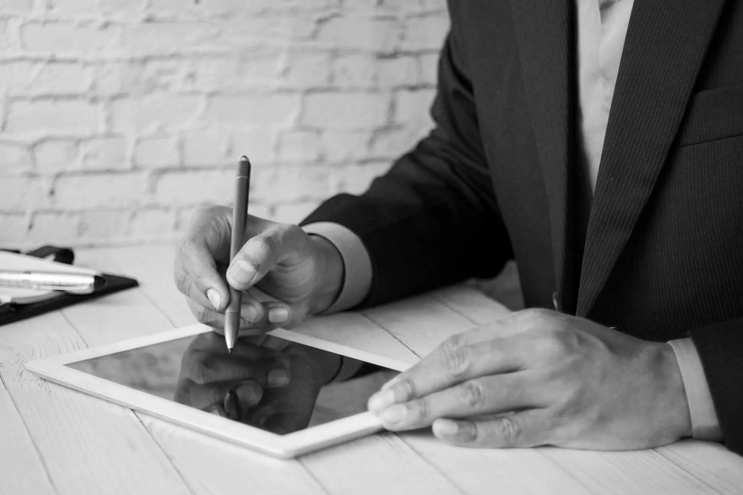 A man in a business suit using a stylus on a tablet at a desk.