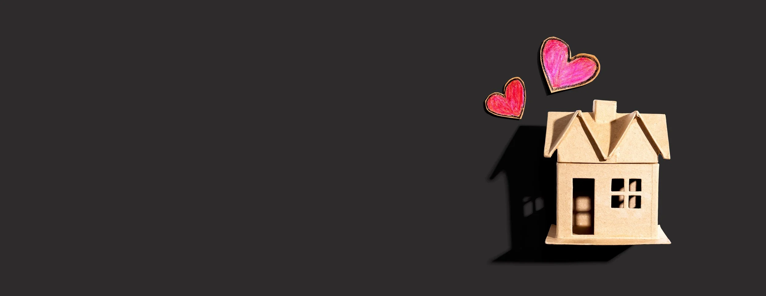 Small wooden house model with colored chalk hearts floating above on black background.