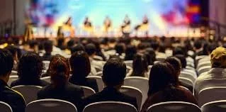 Audience watching a stage performance in a large theater or conference hall.