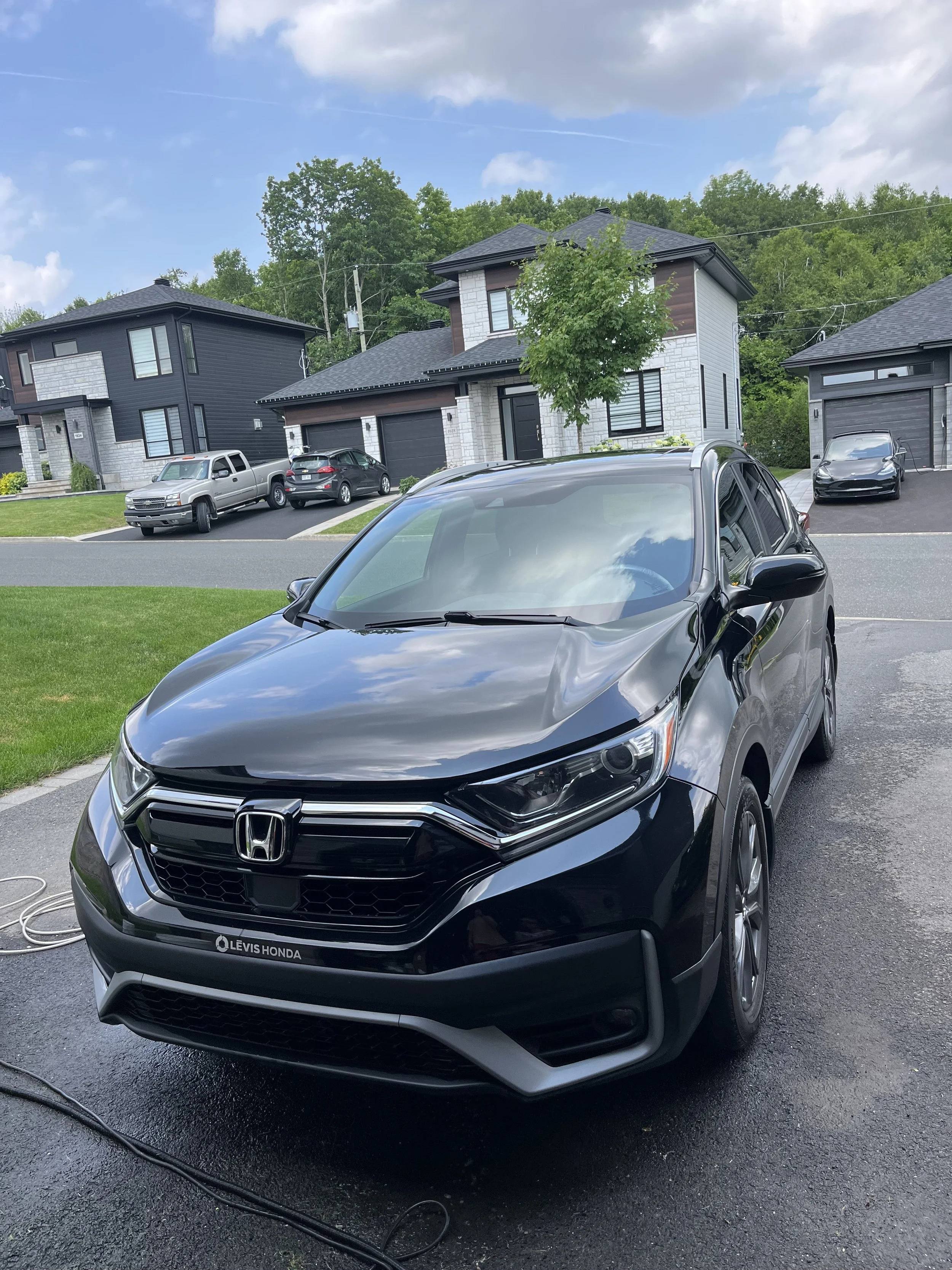 Voiture noire Honda en train d'être lavée devant des maisons modernes dans un quartier résidentiel.