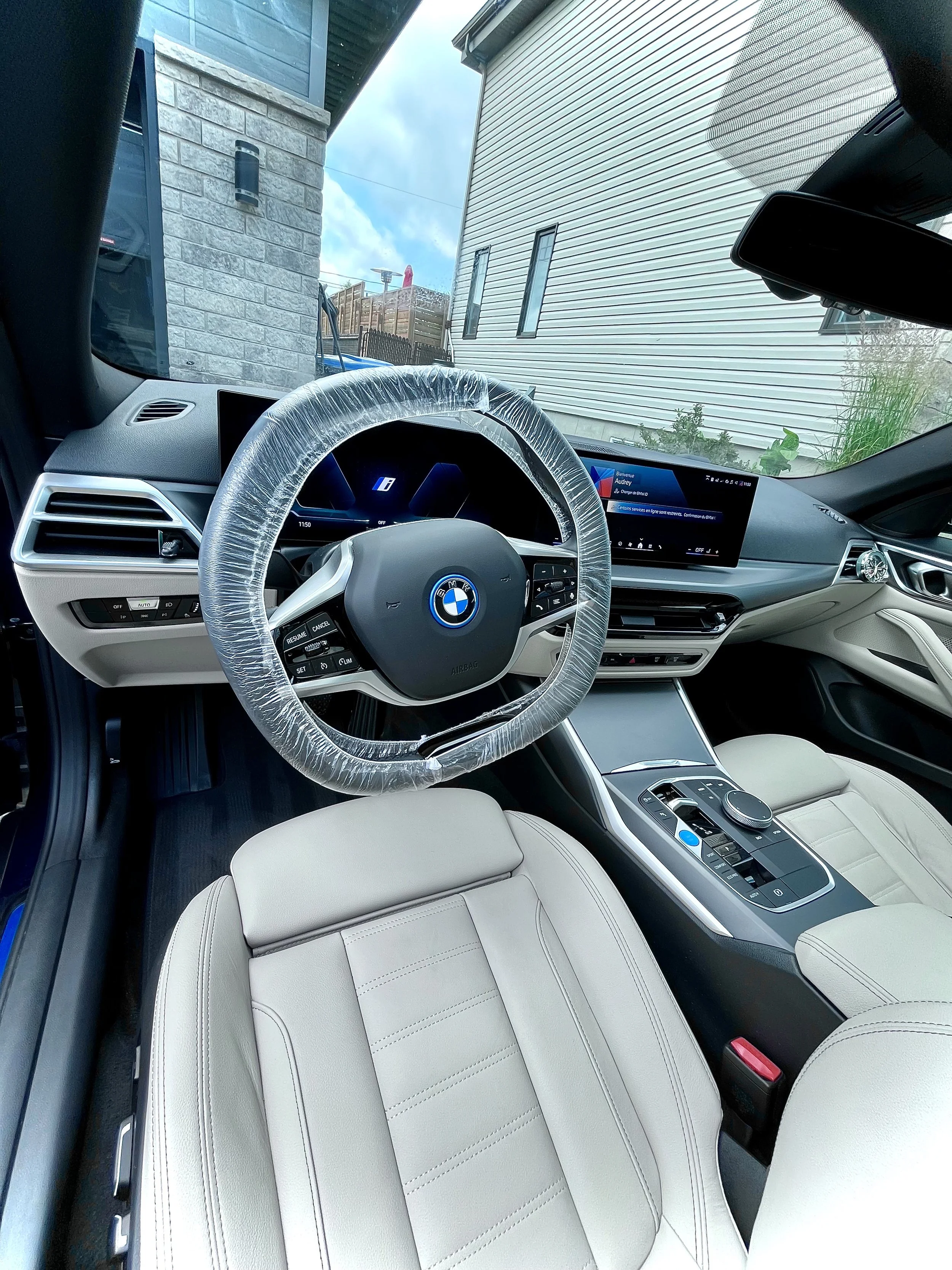 Intérieur d'une voiture BMW moderne avec un tableau de bord numérique, un volant enveloppé dans un plastique protecteur, et un écran d'infodivertissement.