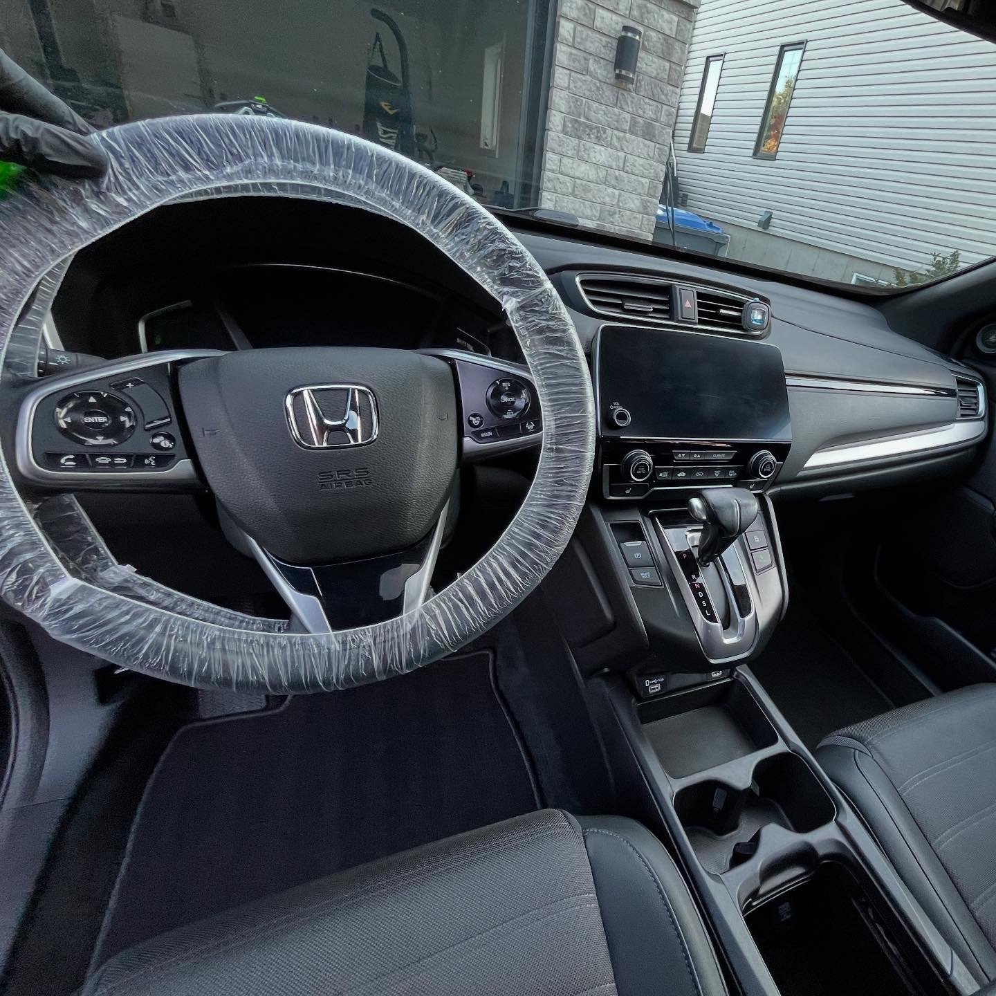Intérieur d'un véhicule Honda avec volant enveloppé d'un plastique, tableau de bord noir, écran central, levier de vitesse automatique, et espace de rangement.