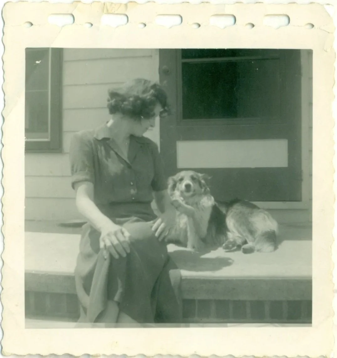 sepia toned snapshot of grandma sitting on a porch stoop in a summer dress turning away from camera to look at her dog that's reaching out for her